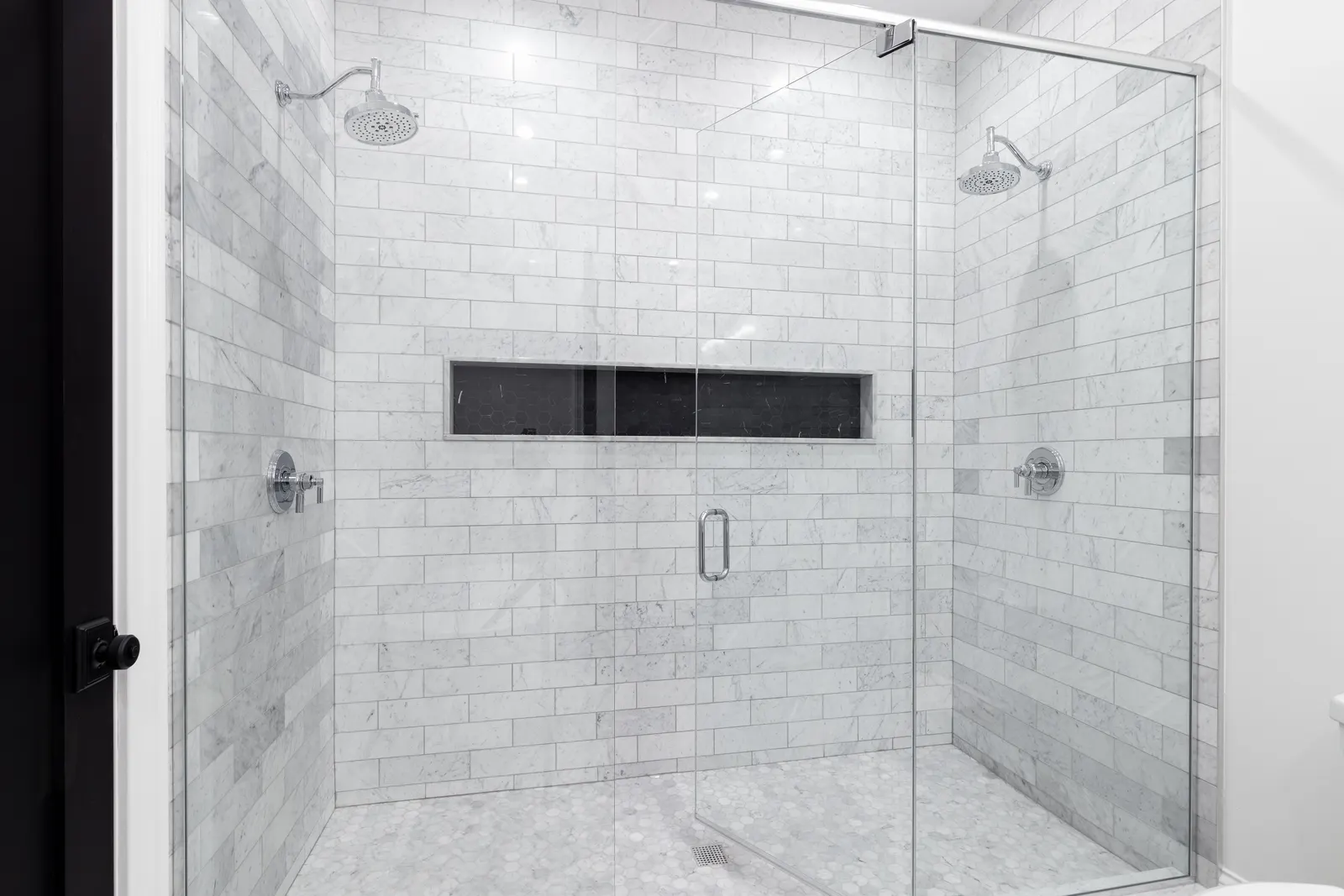 Frameless sliding glass shower doors with dual showerheads and marble subway tile.