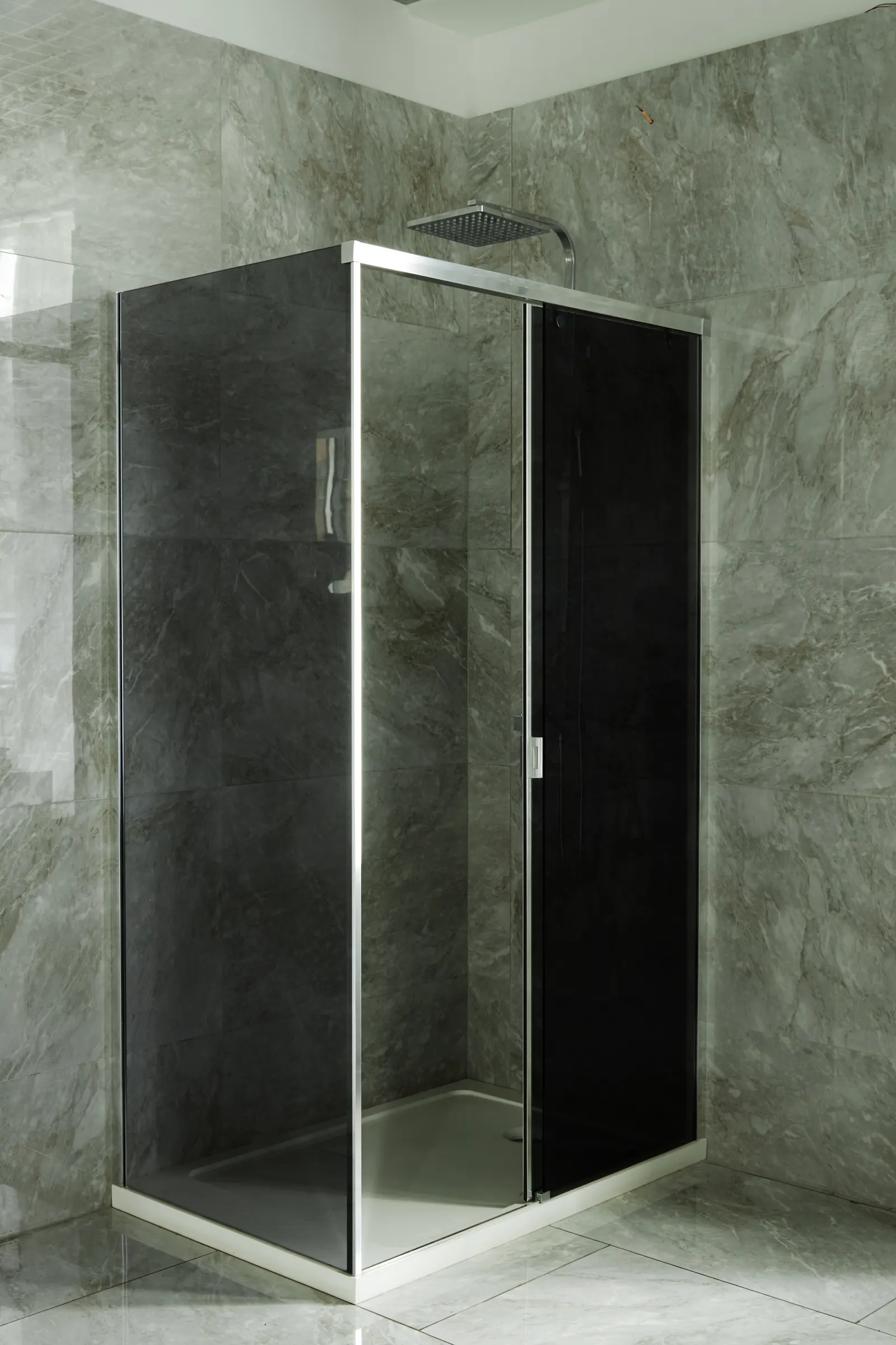Sliding shower enclosure with a tinted glass panel and chrome frame against grey marble tile.