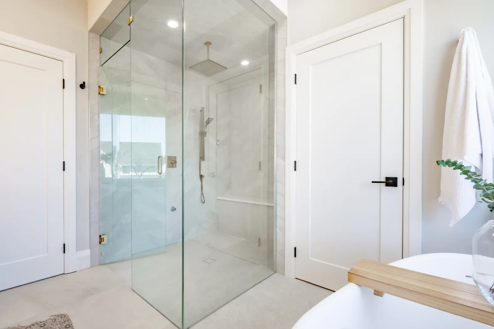 Frameless corner glass shower enclosure with a rain head and built-in bench in a white bathroom.