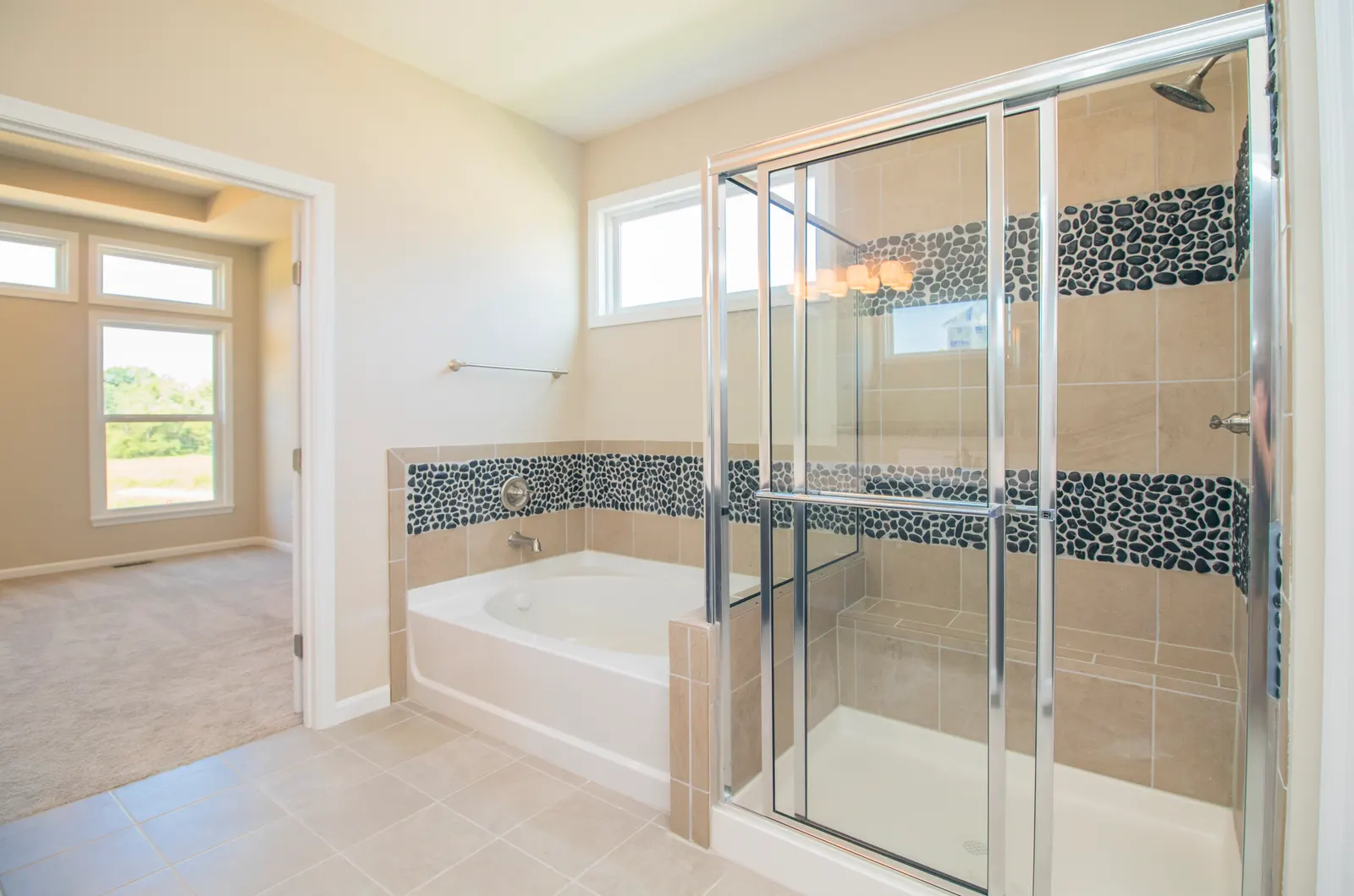 Corner soaking tub beside a framed glass shower with pebble accent tile.