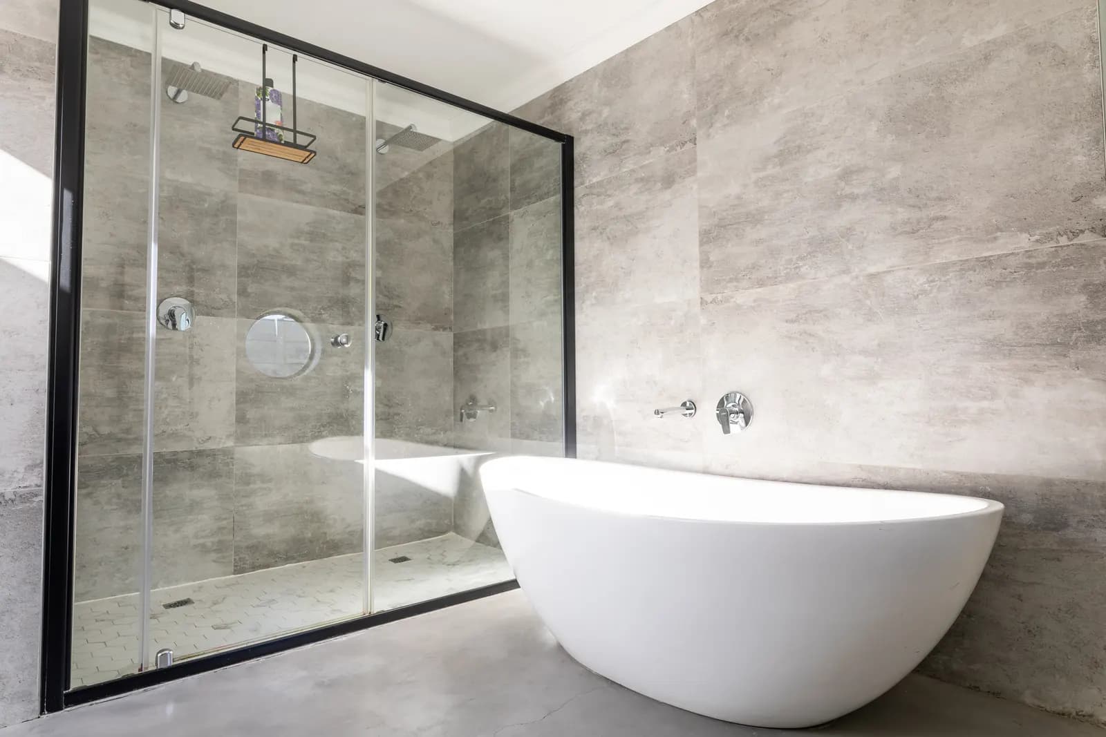 Freestanding tub beside a black-framed sliding glass shower with concrete-look tile.