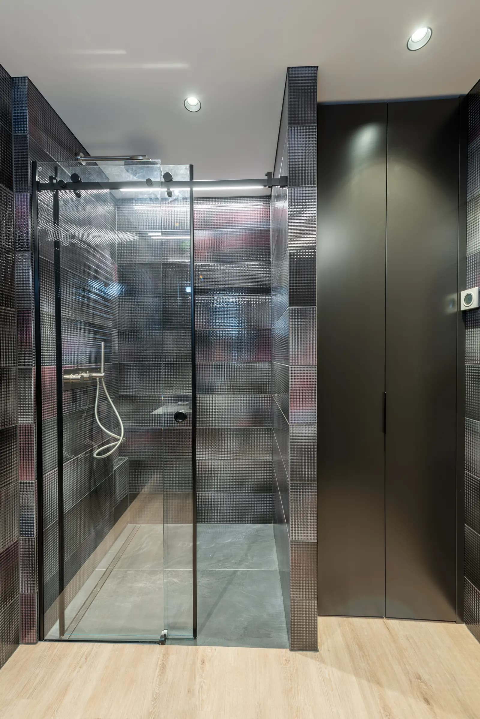 Sliding shower door with reeded textured glass and a black frame in a dark bathroom.