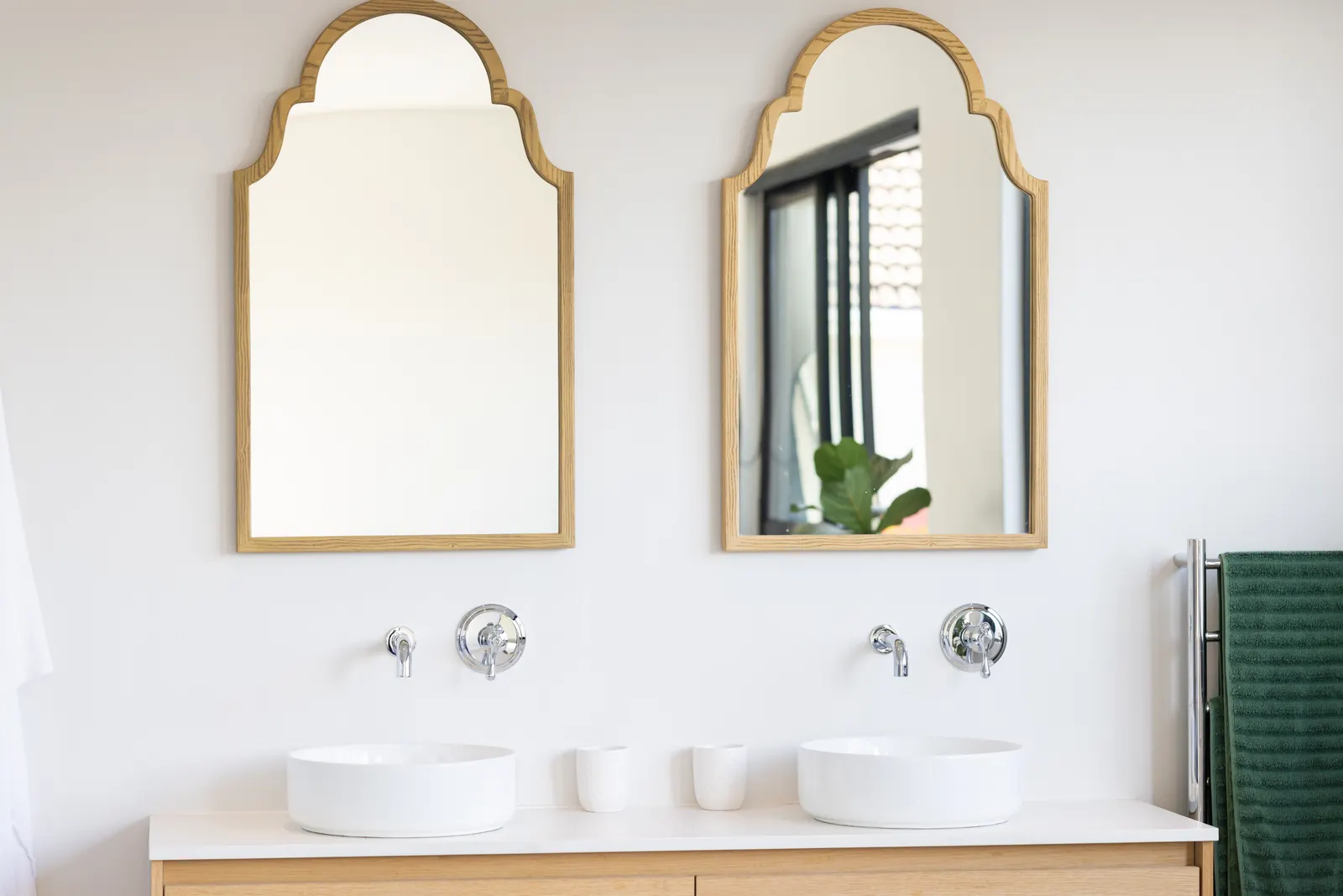 Two arched wood-framed mirrors above a double vanity with white vessel sinks and chrome taps.