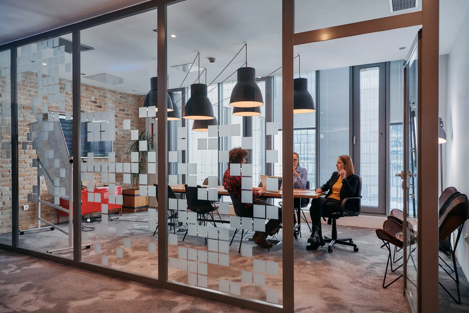 People meeting in a glass-partitioned room with a frosted square pattern.
