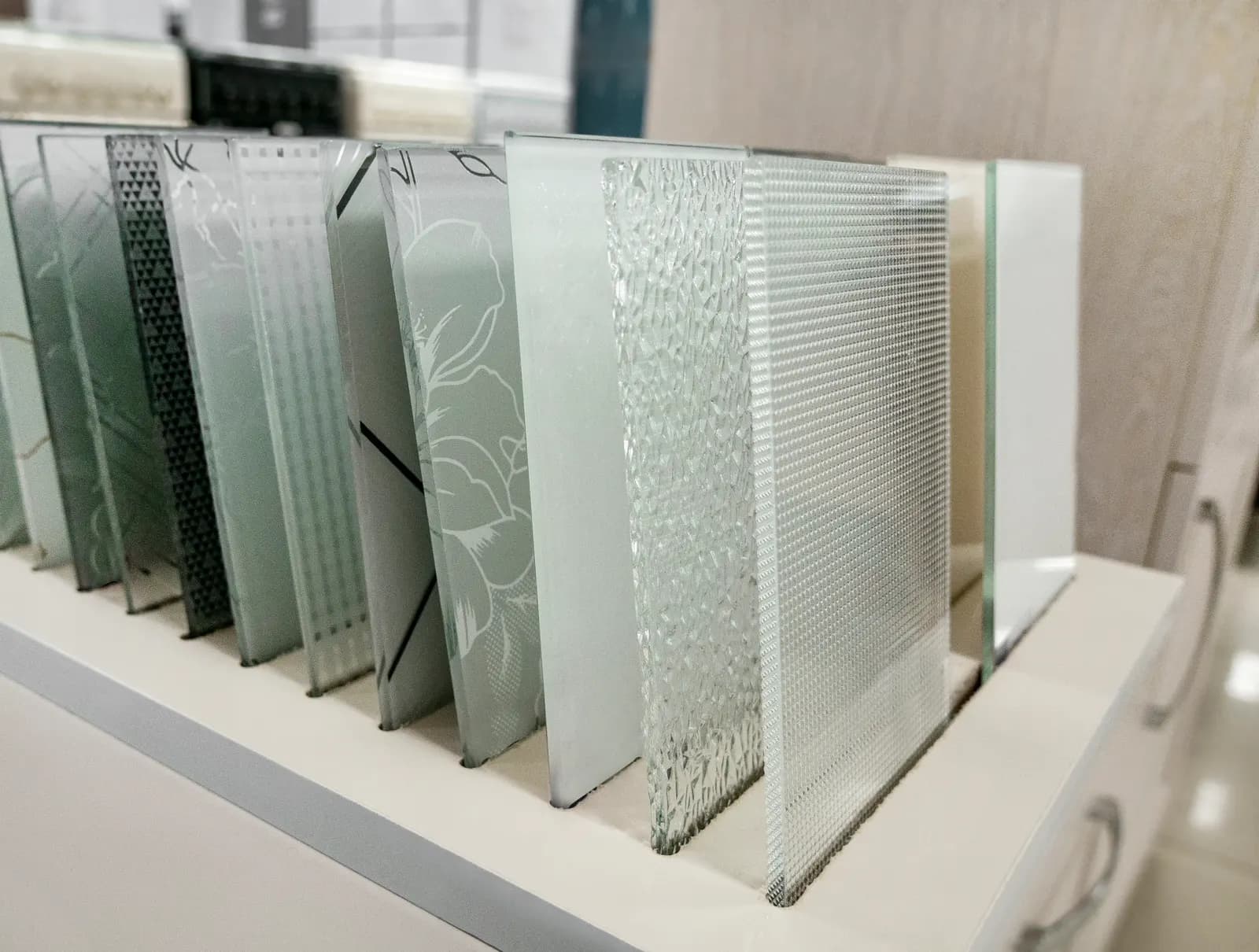 Upright samples of patterned and textured decorative glass displayed on a shelf.