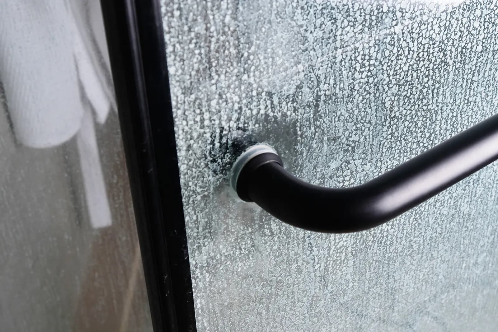 Close-up of a matte black handle on a water-spotted glass shower door.