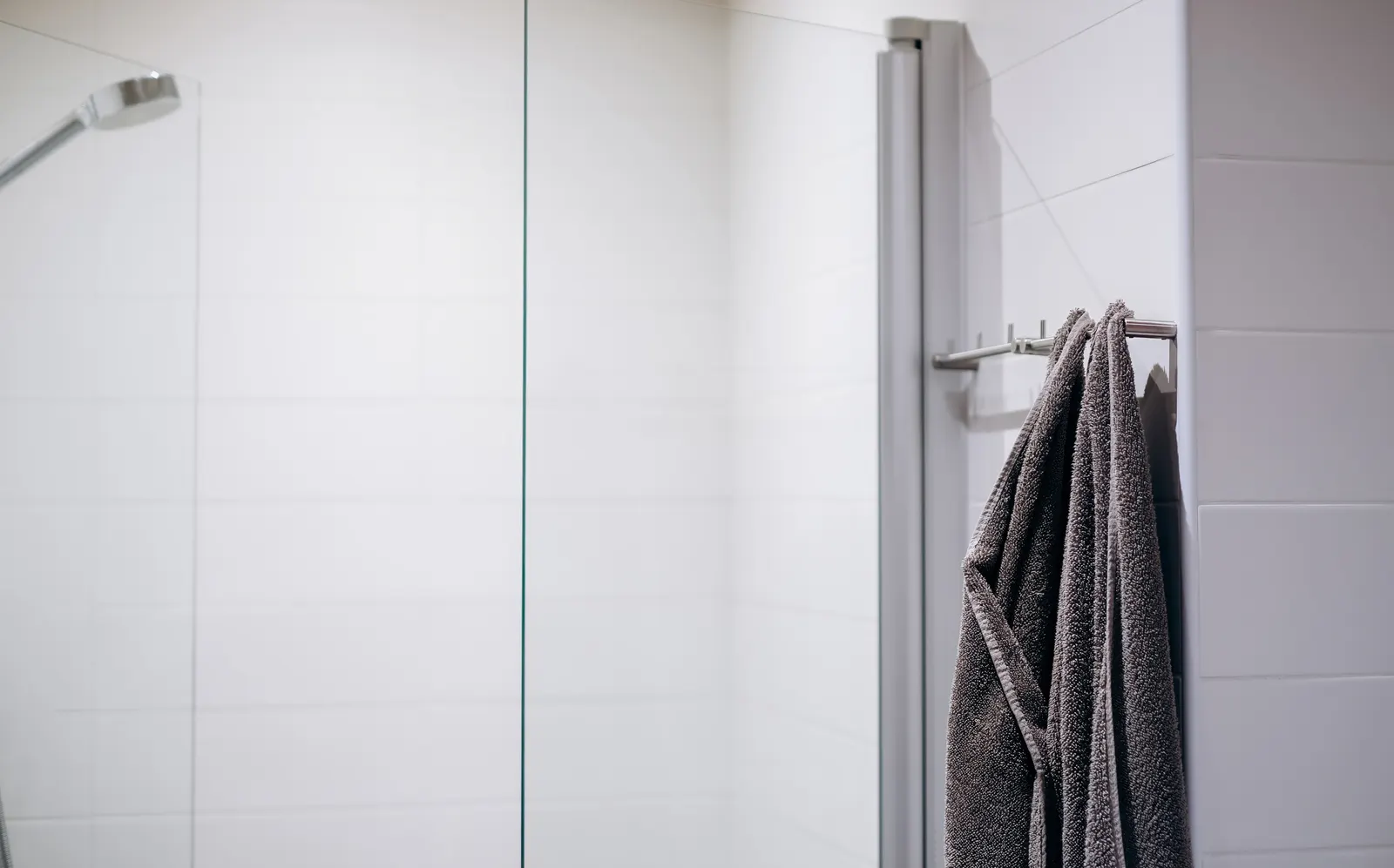 Glass shower screen beside a white-tiled wall with towels on a chrome rail.