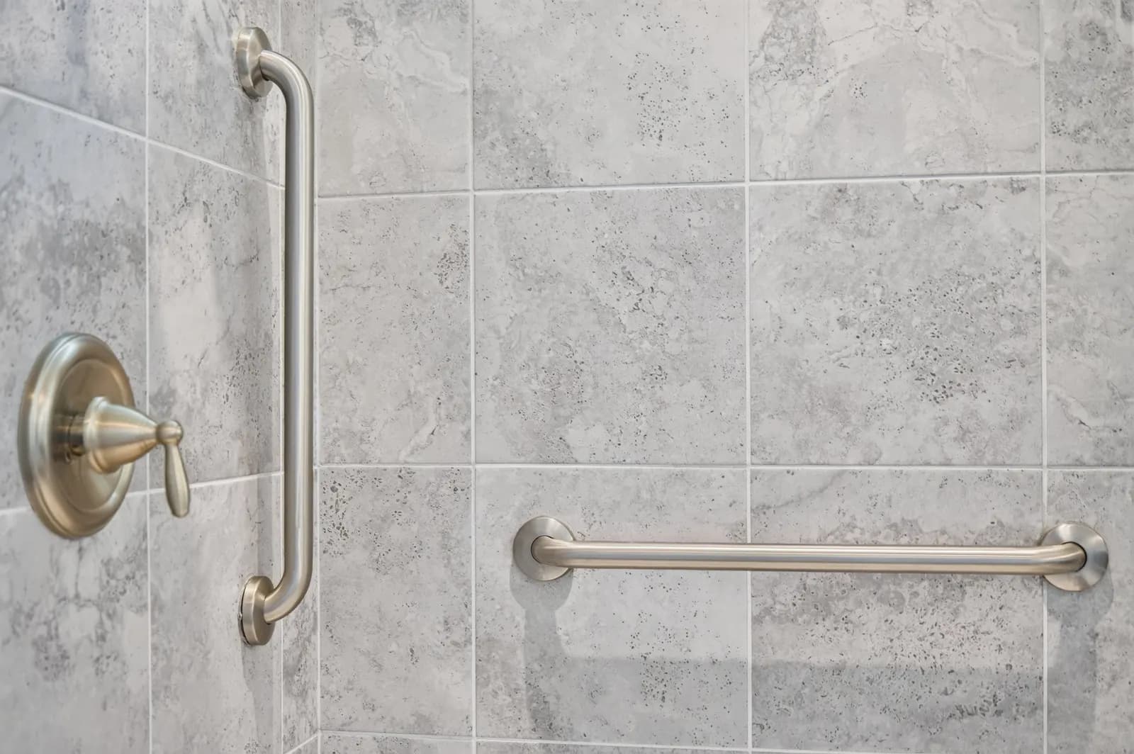 Brushed nickel grab bars and a shower valve on a grey tiled wall.