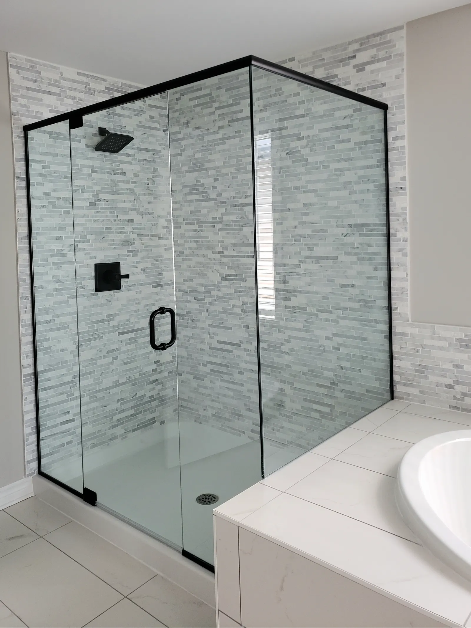 Black-framed corner glass shower enclosure with a hinged door and marble mosaic tile.