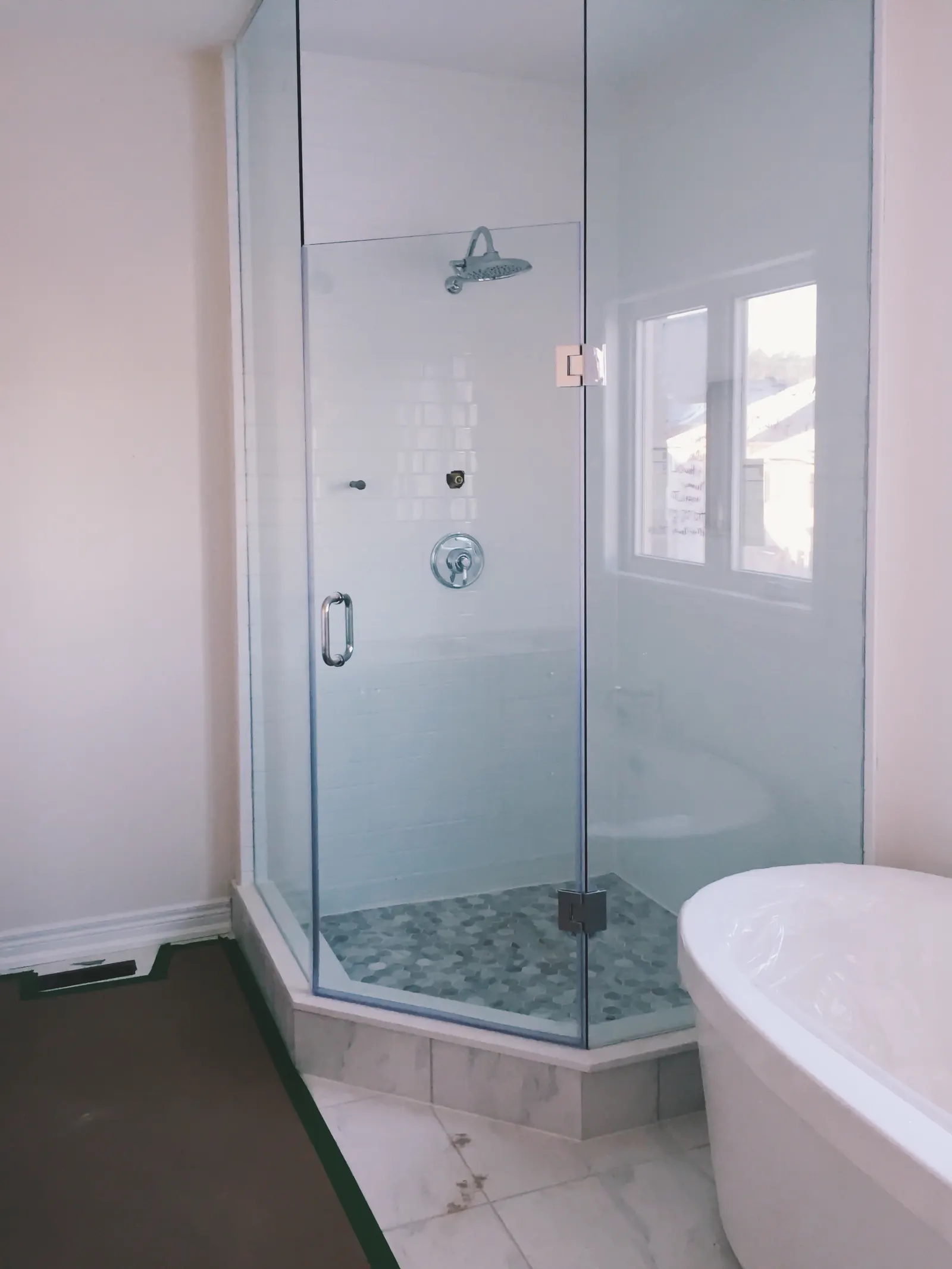 Frameless neo-angle glass shower enclosure with chrome hinges beside a freestanding tub.