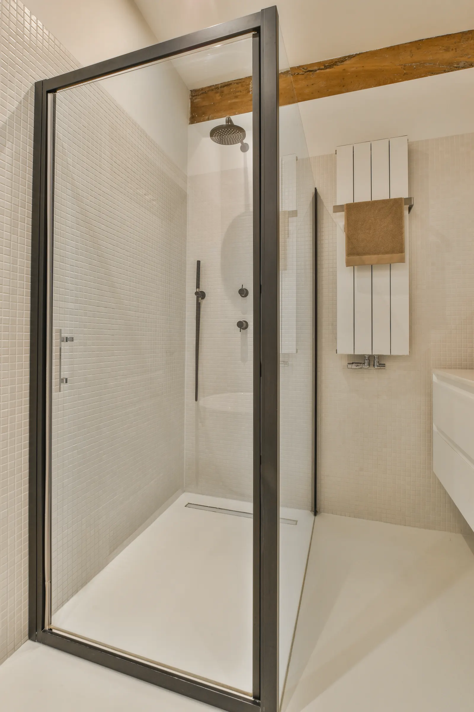 Bronze-framed hinged glass shower enclosure in a white mosaic-tiled bathroom.