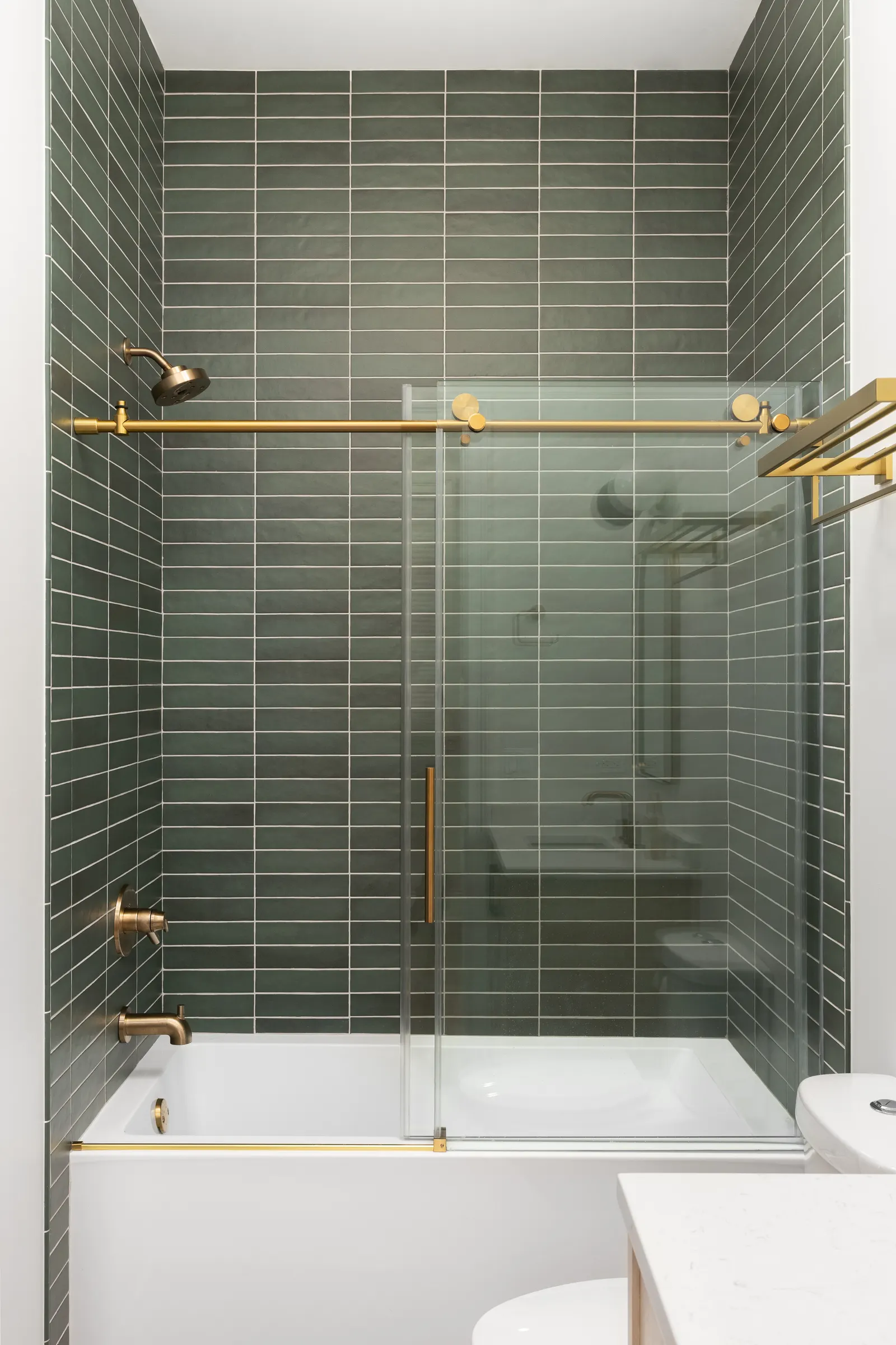 Sliding glass tub screen with brushed brass hardware over a white bathtub and green tile.