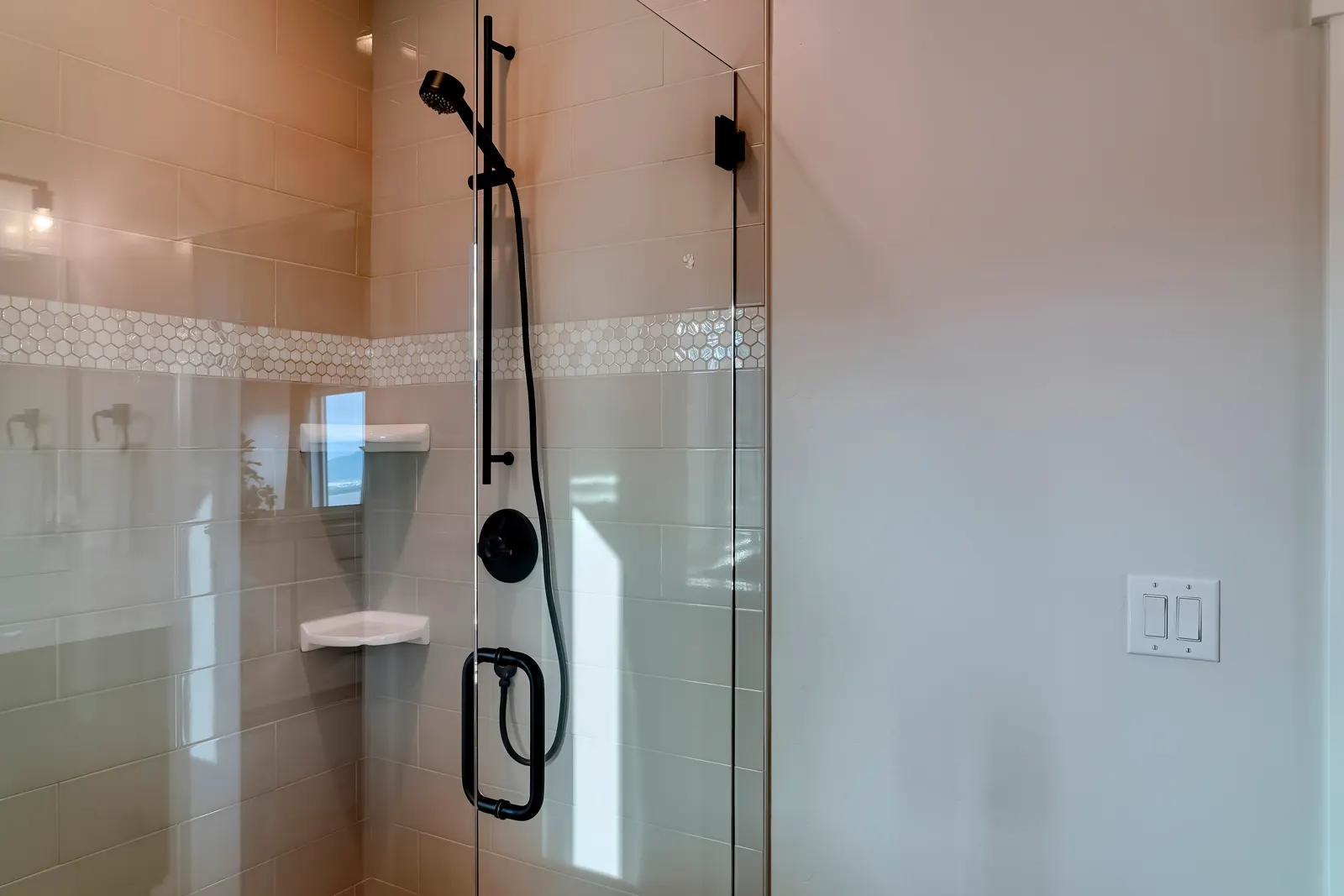 Frameless glass shower panel with matte black hardware against beige subway tile.