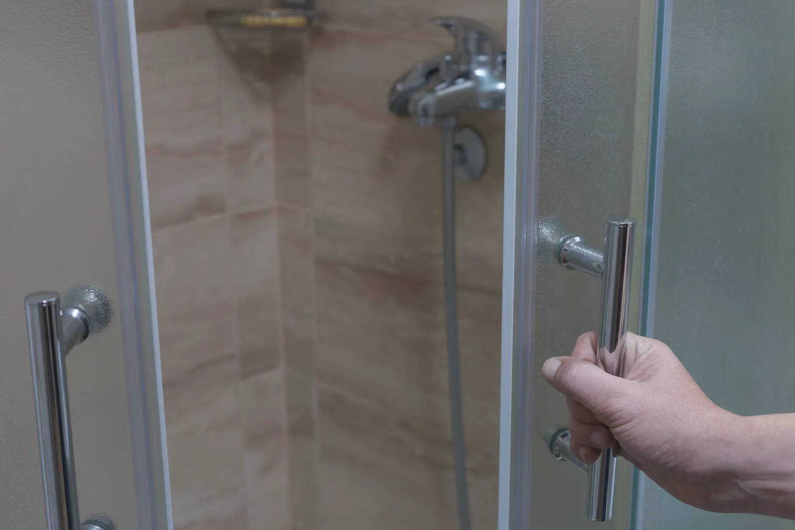 Hand opening a framed frosted-glass shower door by its chrome bar handle.