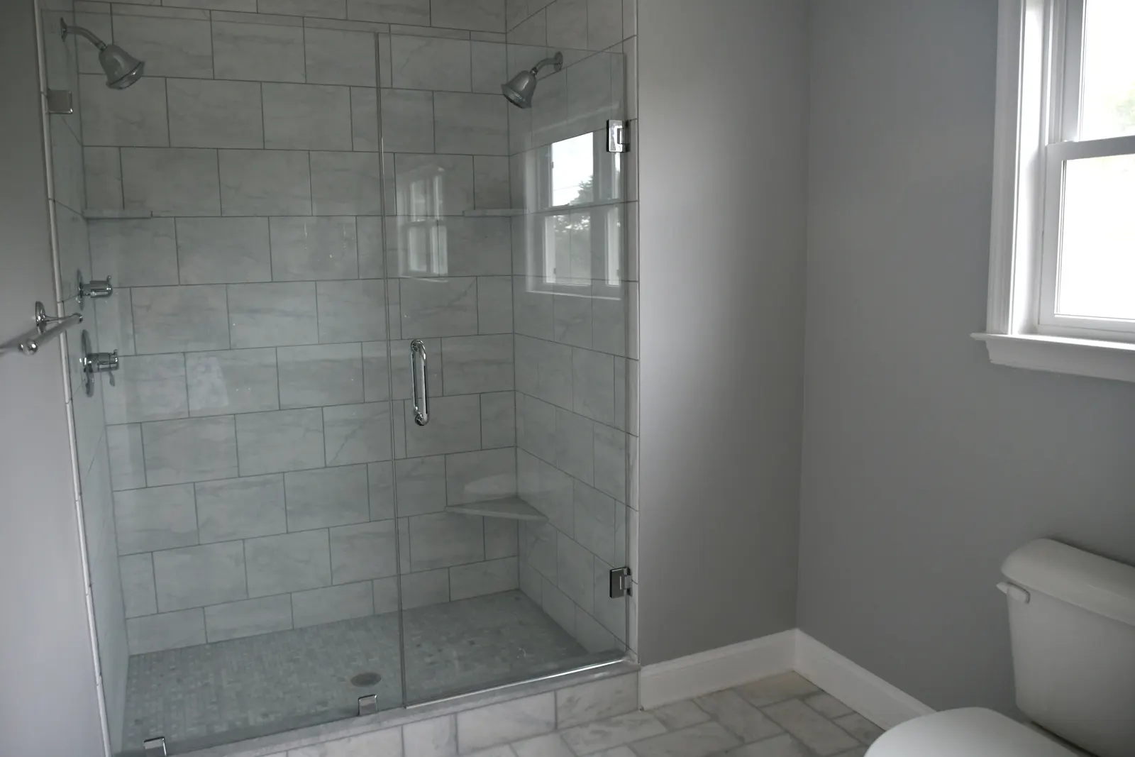 Frameless glass shower door with a chrome handle against white marble tile.