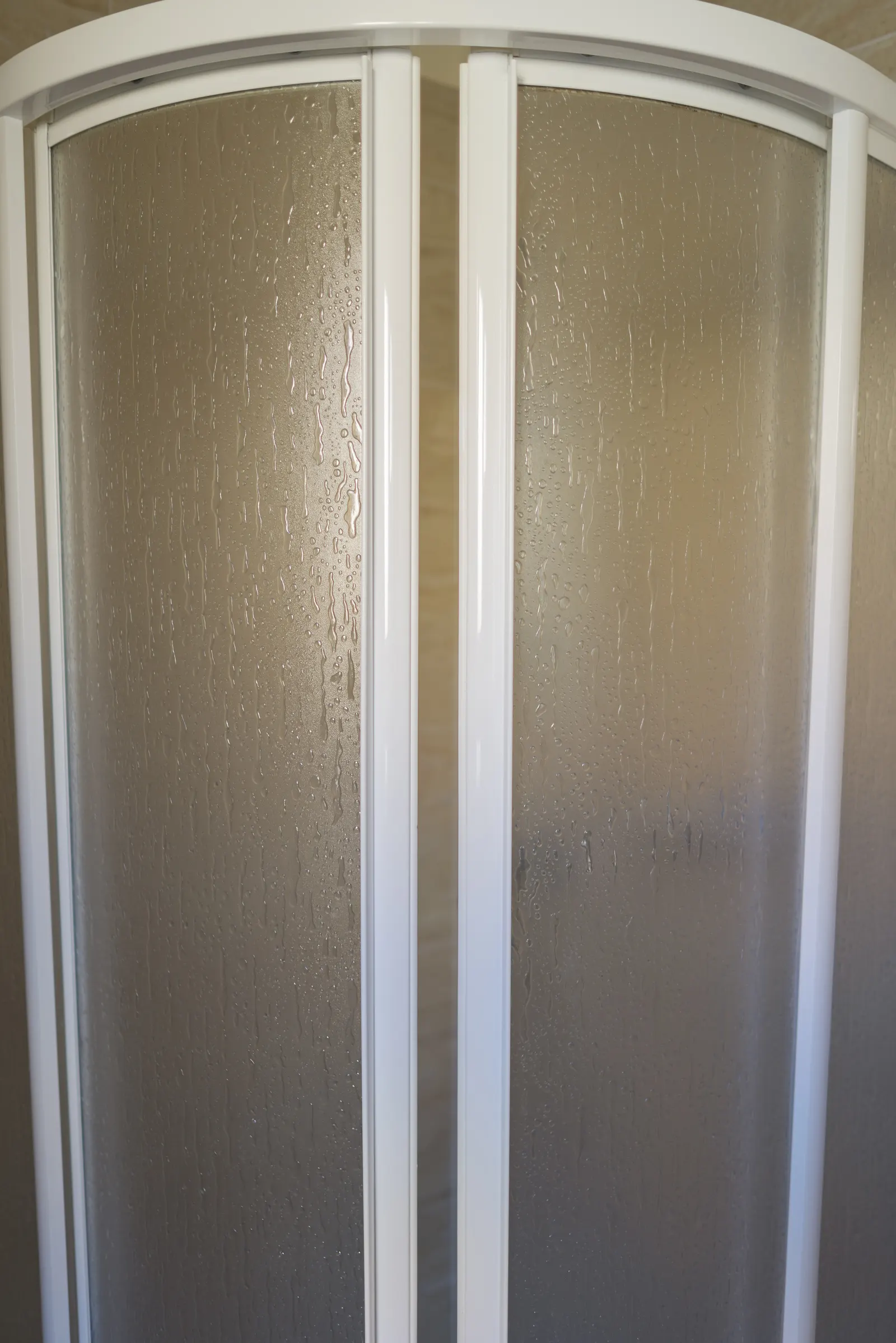 White-framed curved sliding shower doors with water-spotted pebbled glass.