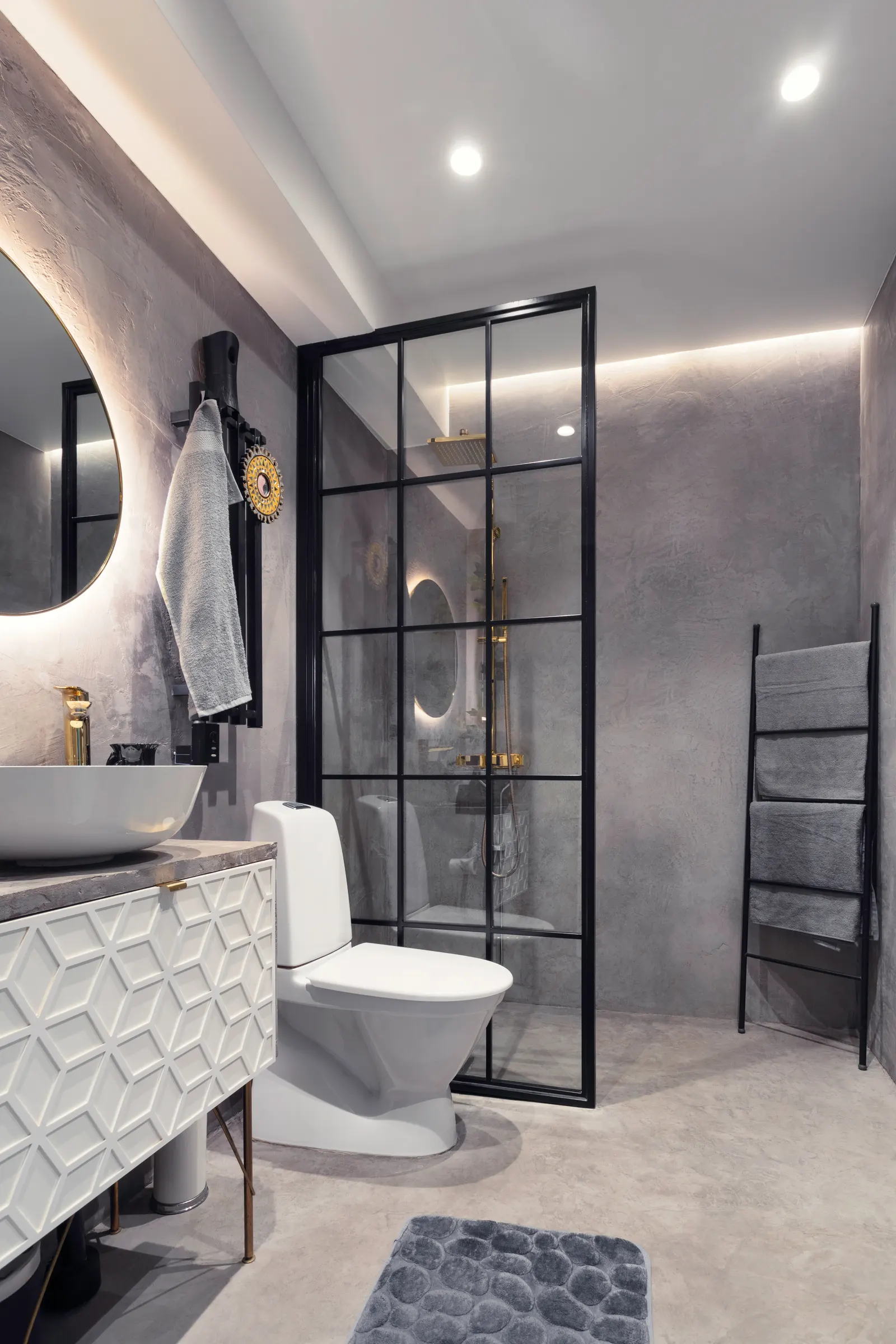 Black grid-framed fixed glass shower screen with brass fixtures in a grey concrete bathroom.
