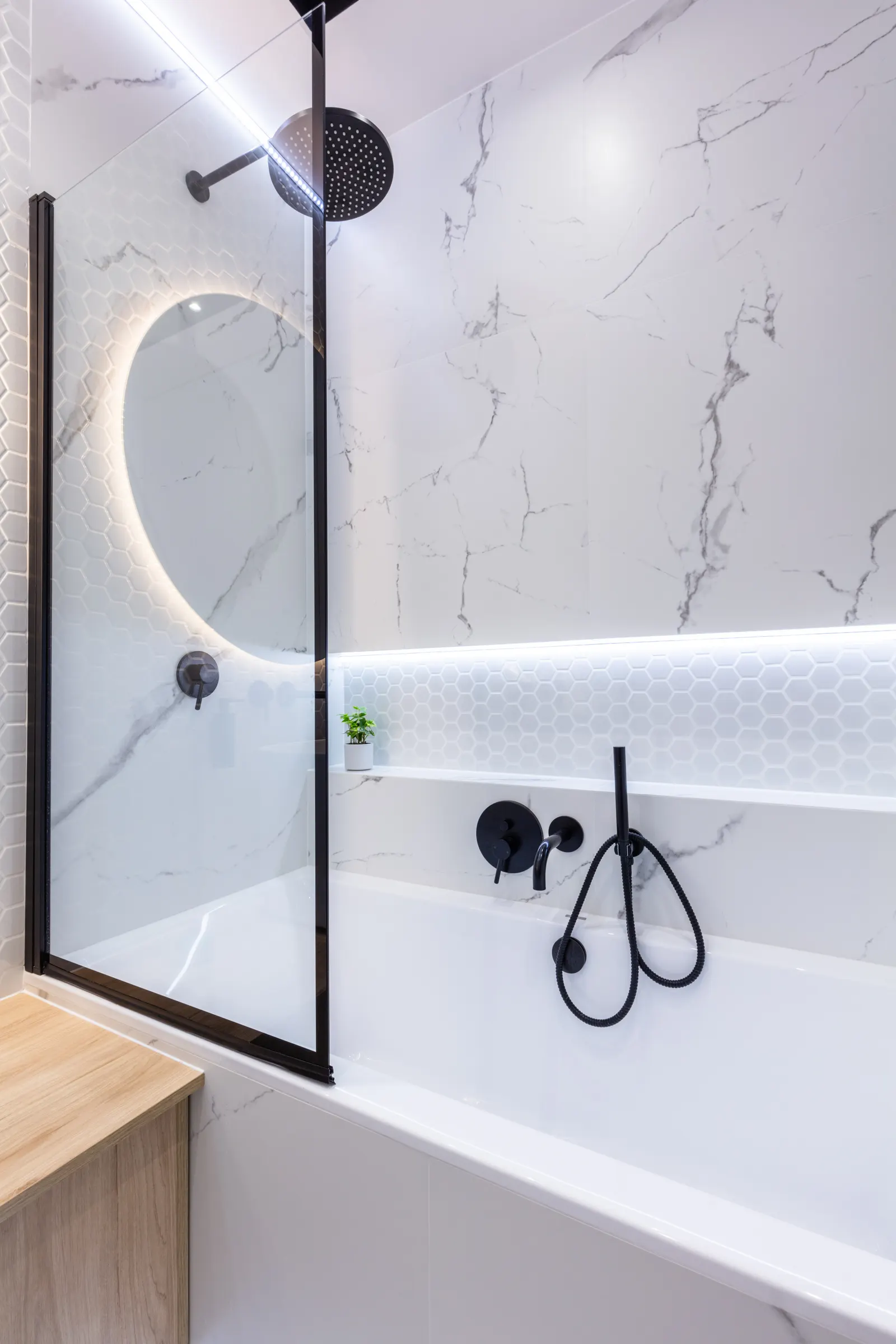Bathtub with a black-framed fixed glass bath screen and white marble tile.