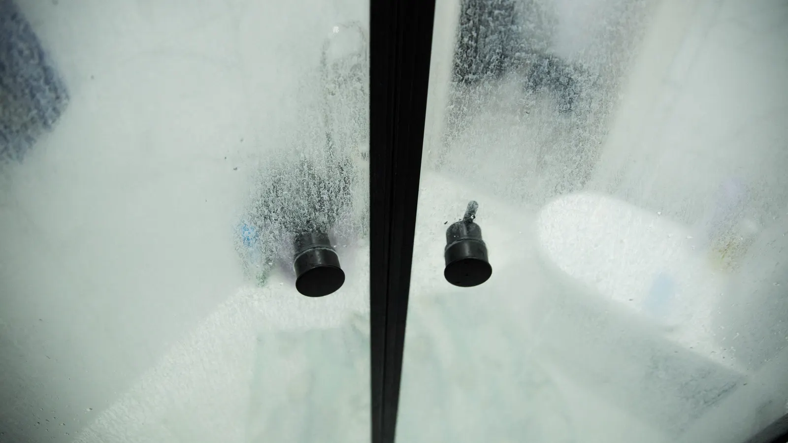Close-up of guide bumpers on a fogged sliding glass shower door.