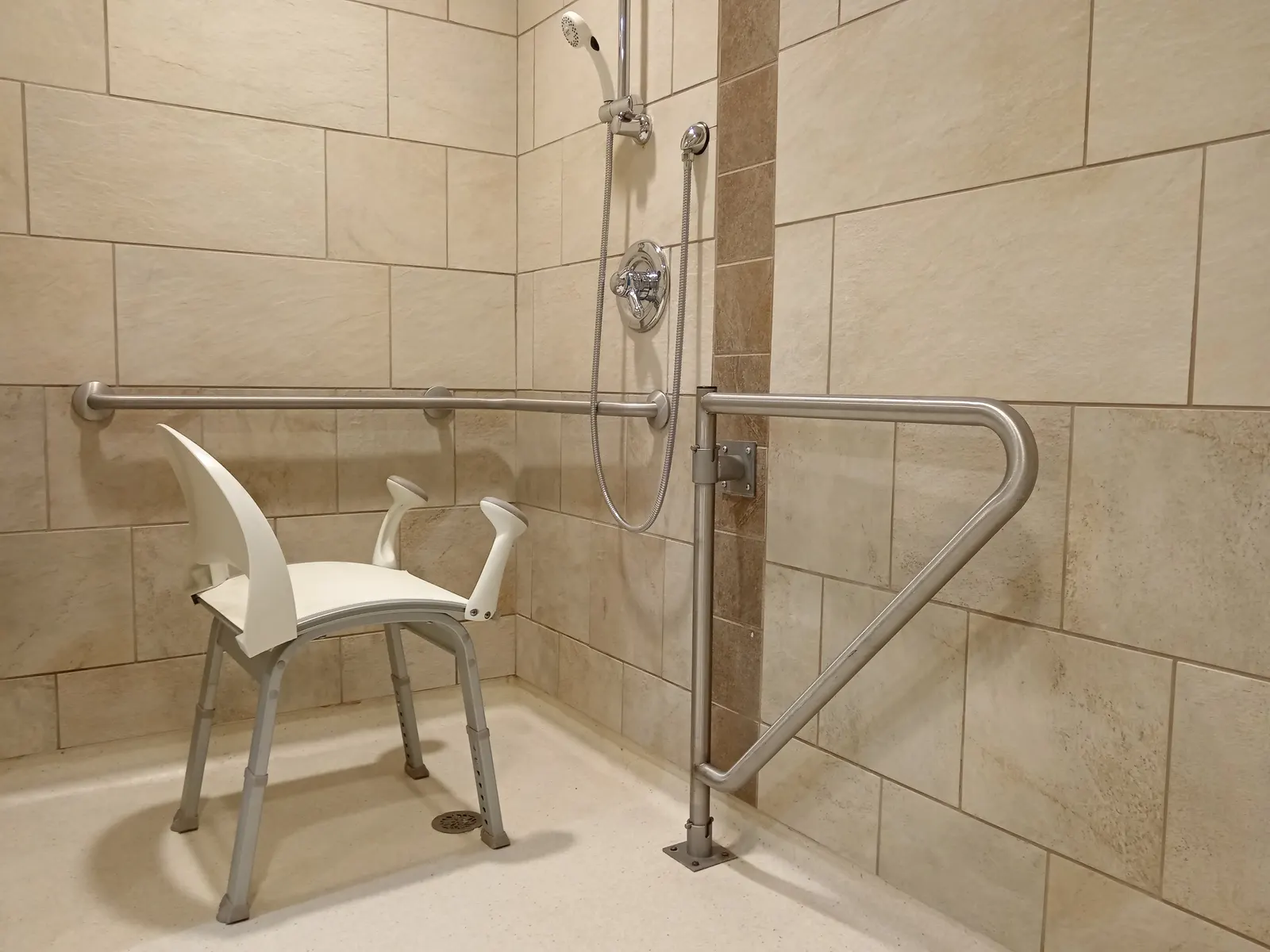 Accessible roll-in shower with a portable shower chair, grab bars, and a handheld shower.