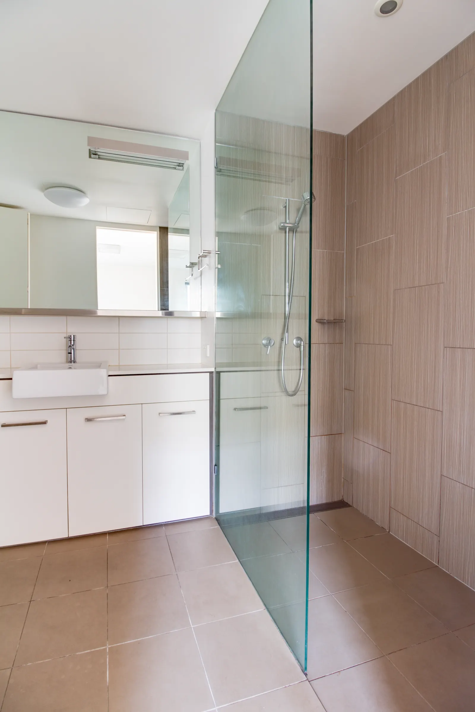 Curbless walk-in shower with a fixed frameless glass panel and wood-look tile.