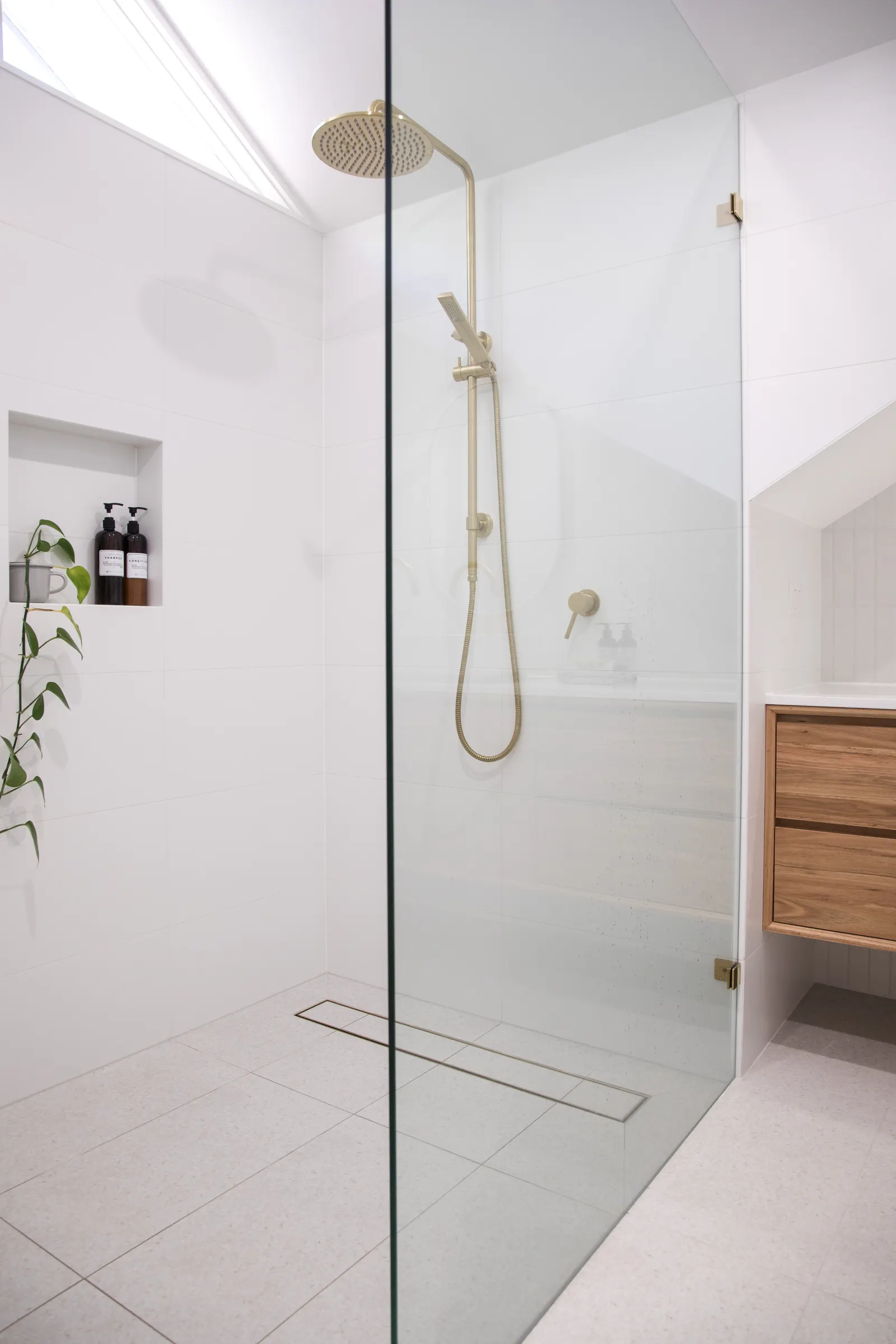 Curbless walk-in shower with a fixed glass panel, linear drain, and gold rain head.