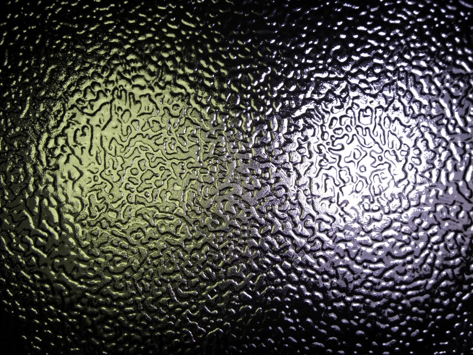 Close-up of dark textured obscure glass lit with green and white light.