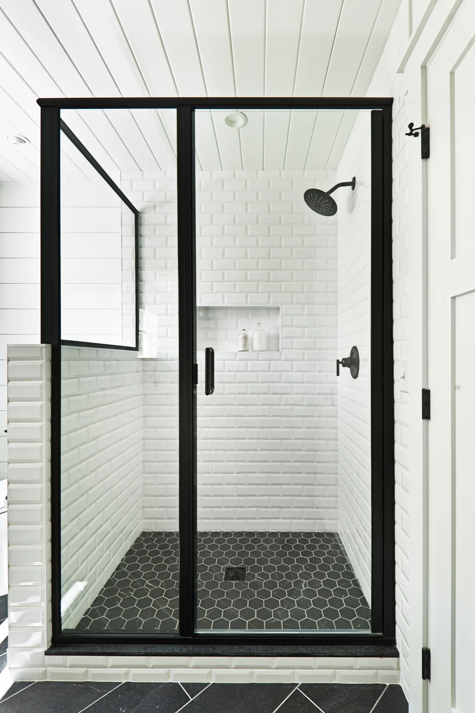 Walk-in shower with a black-framed glass hinged door and white subway tile.