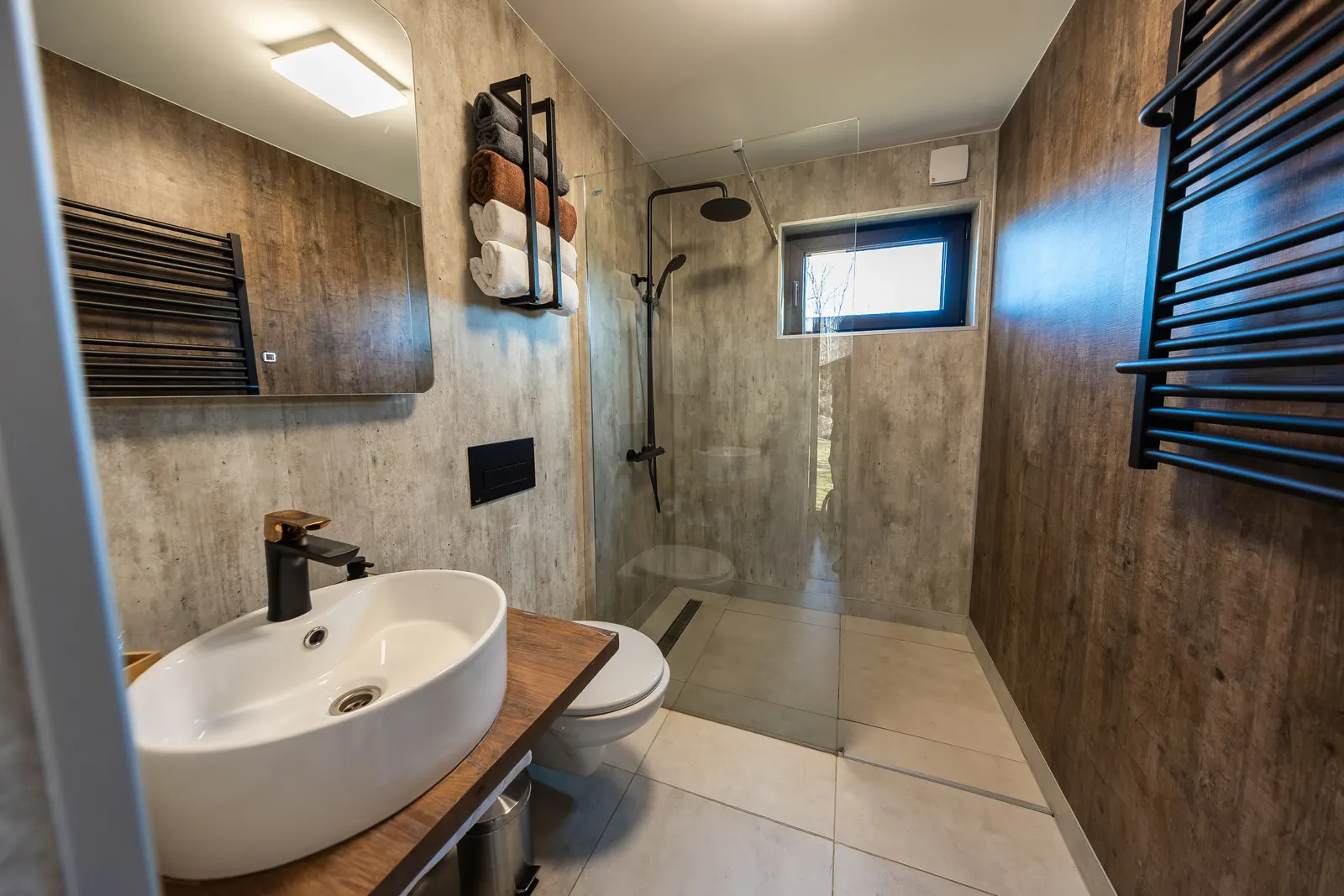 Walk-in shower with a single fixed glass panel and black fixtures in a wood-look tiled bathroom.
