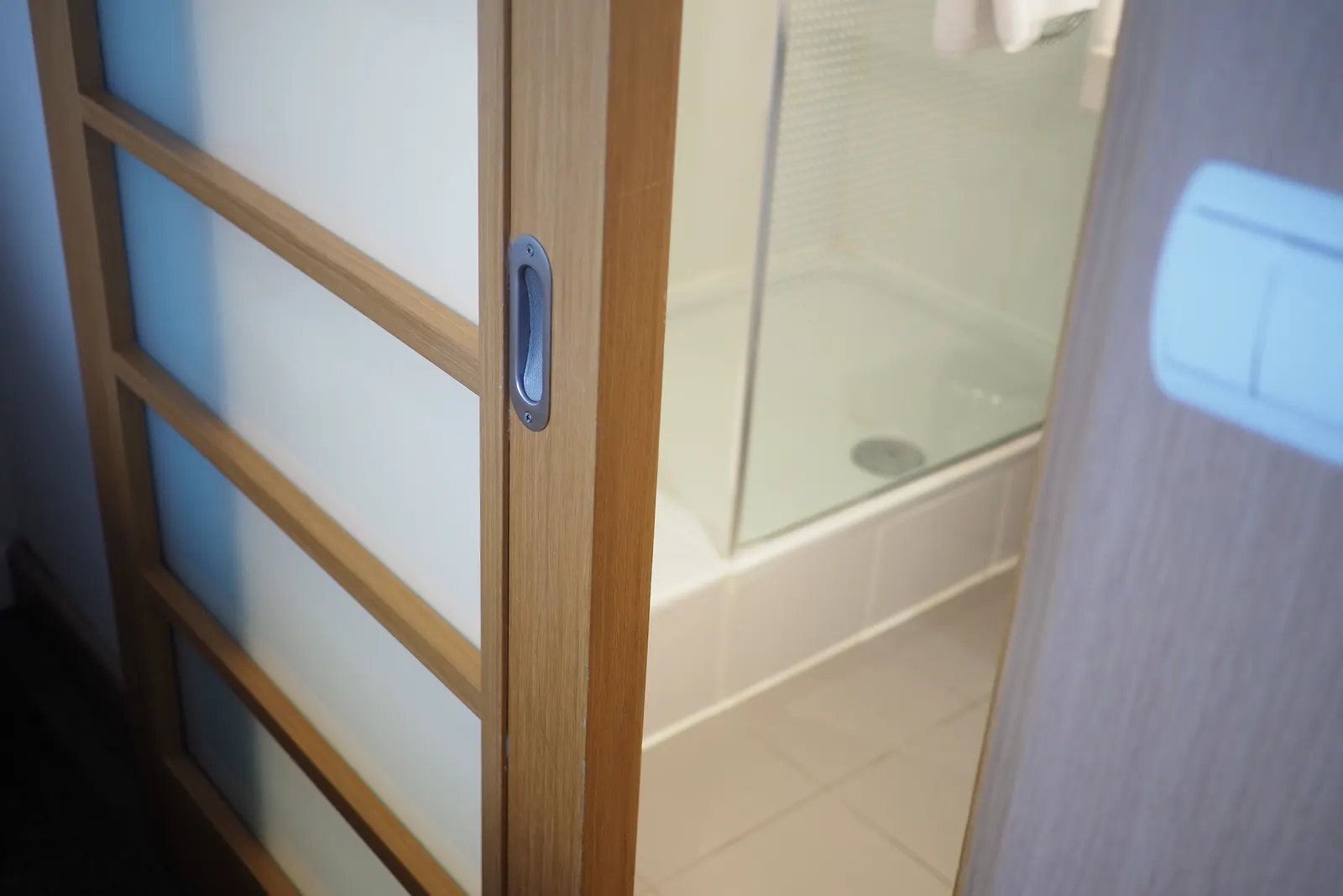 Wood-framed frosted sliding door with a recessed pull opening into a tiled bathroom.