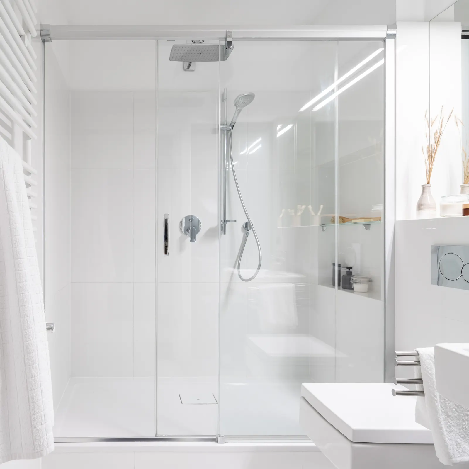 Chrome-framed sliding glass shower door with a fixed panel in an all-white bathroom.