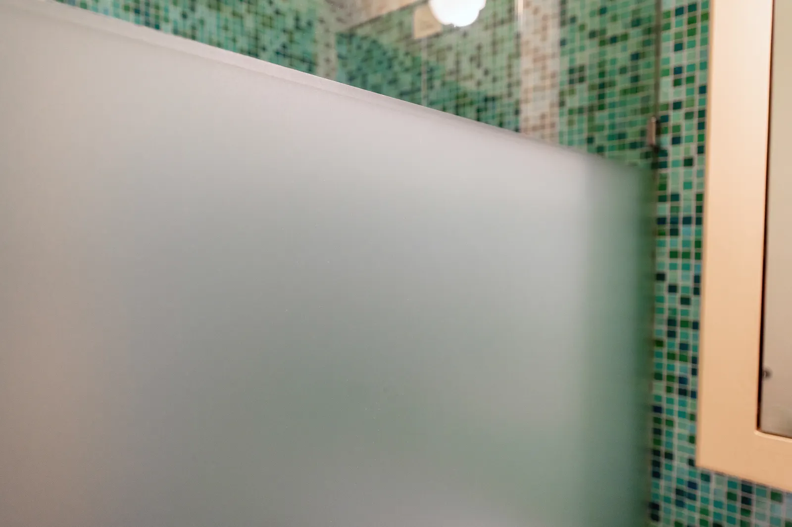 Close-up of a frosted glass shower panel edge with green mosaic tile behind.