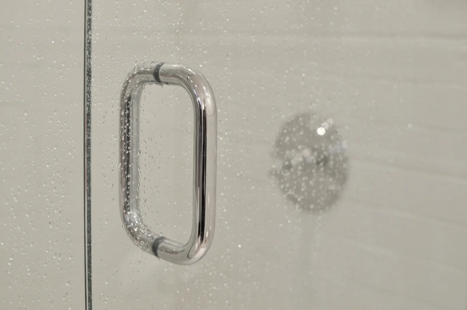Close-up of a chrome pull handle on a water-spotted glass shower door.
