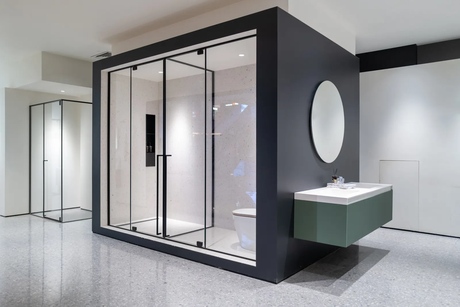 Frameless glass shower enclosure with black hardware and terrazzo interior in a showroom.