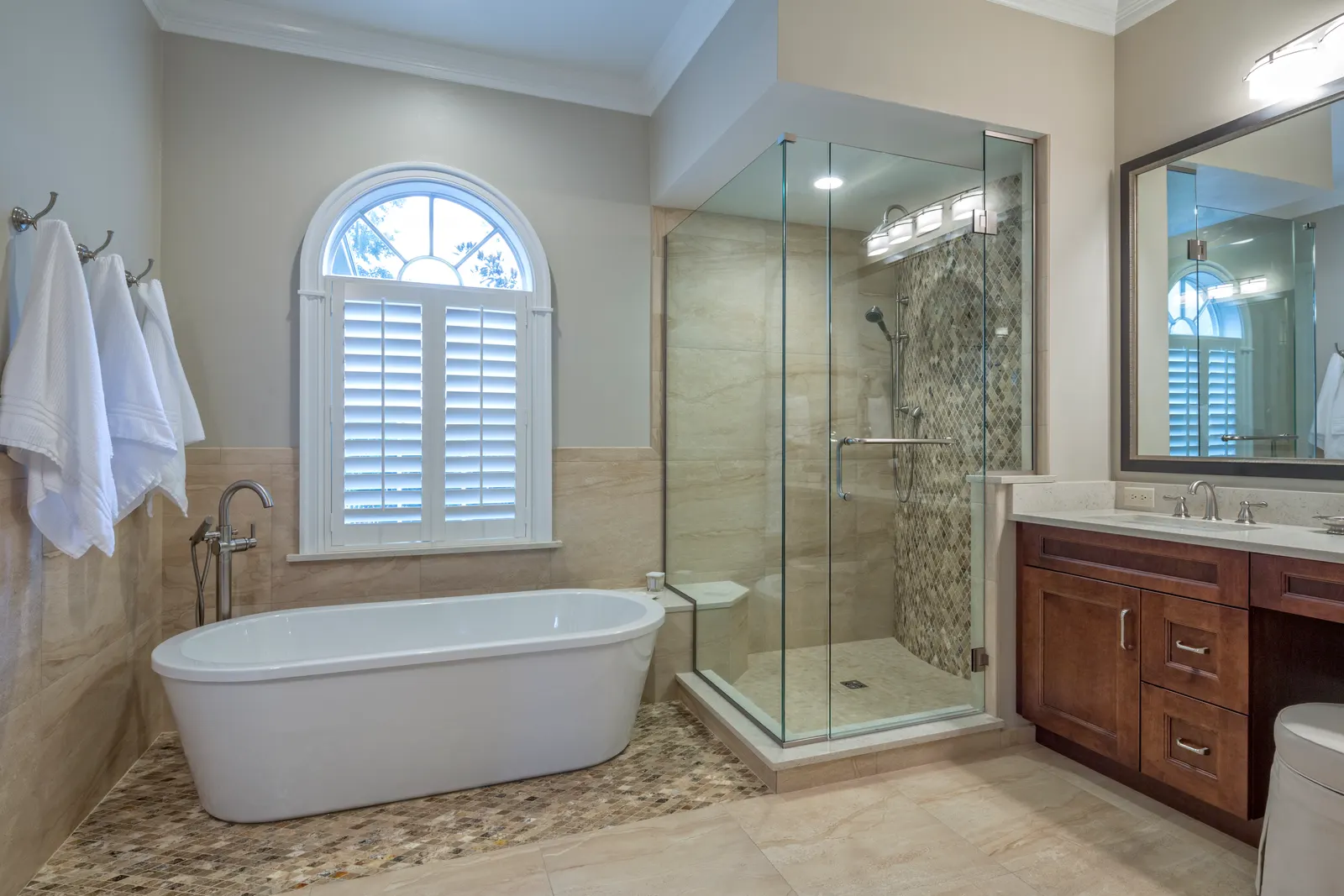 Freestanding tub beside a corner glass shower with a hinged door and arched window.