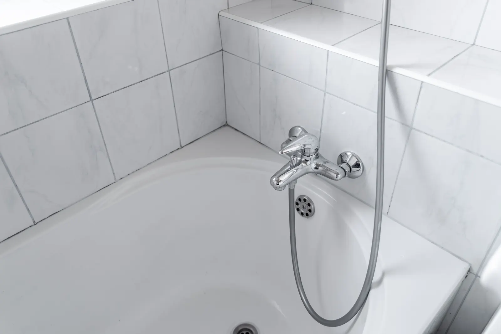 Close-up of a chrome wall-mounted bath faucet and handheld hose over a white tub.