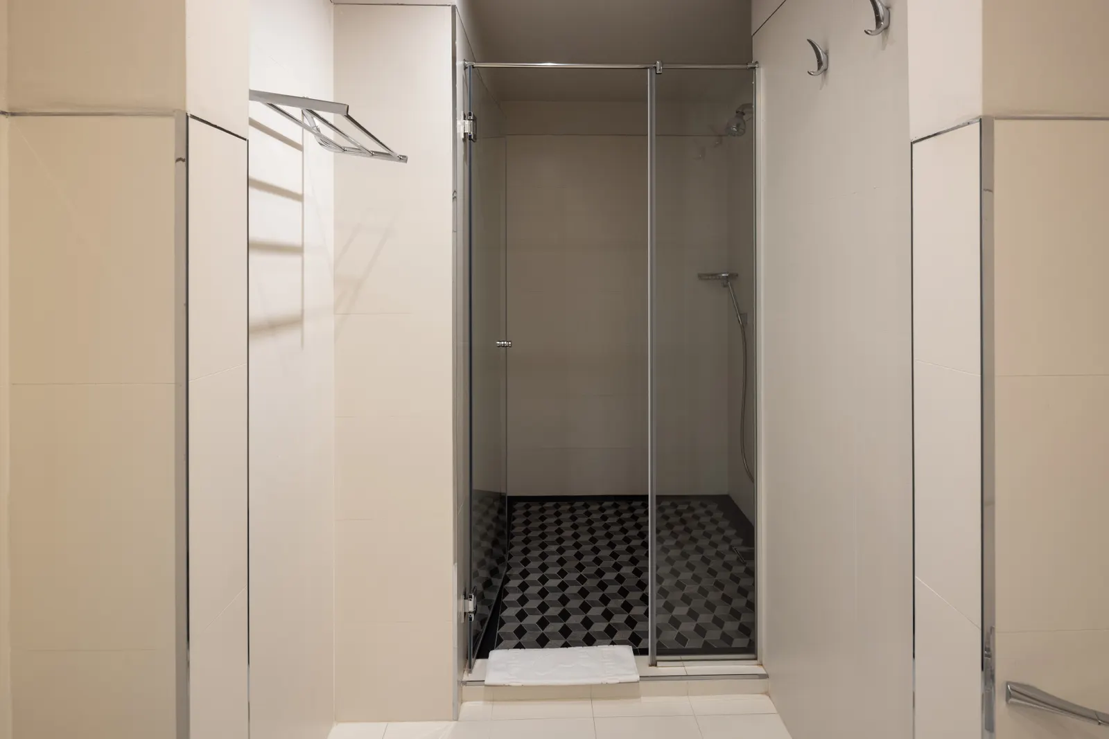 Tiled shower cubicle with a framed glass door and geometric floor tile in a shared washroom.