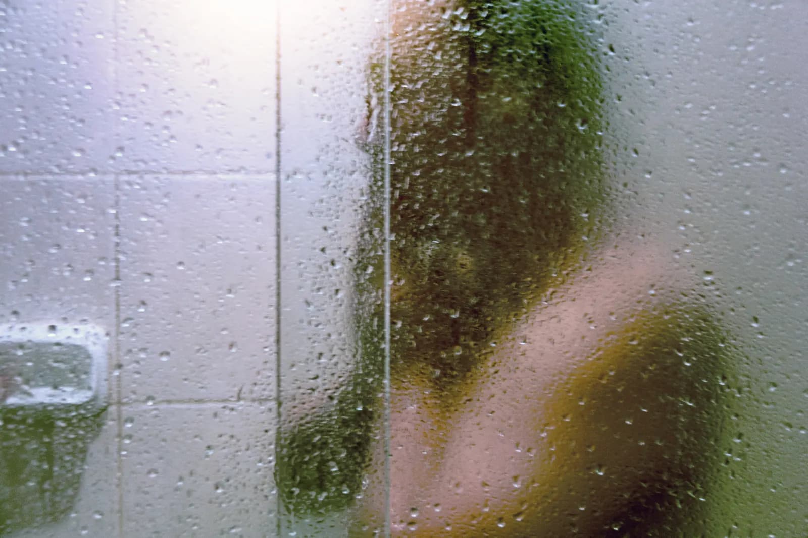 Close-up of a steamy shower glass panel obscuring the blurred silhouette of a person behind it.
