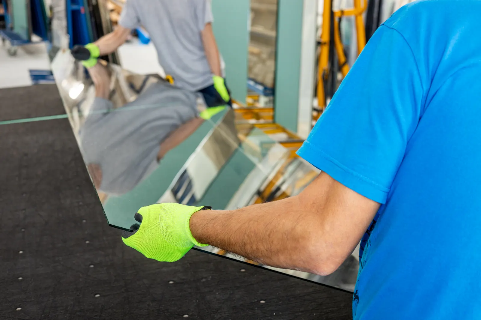 Two workers in gloves handling a large sheet of glass in a workshop.