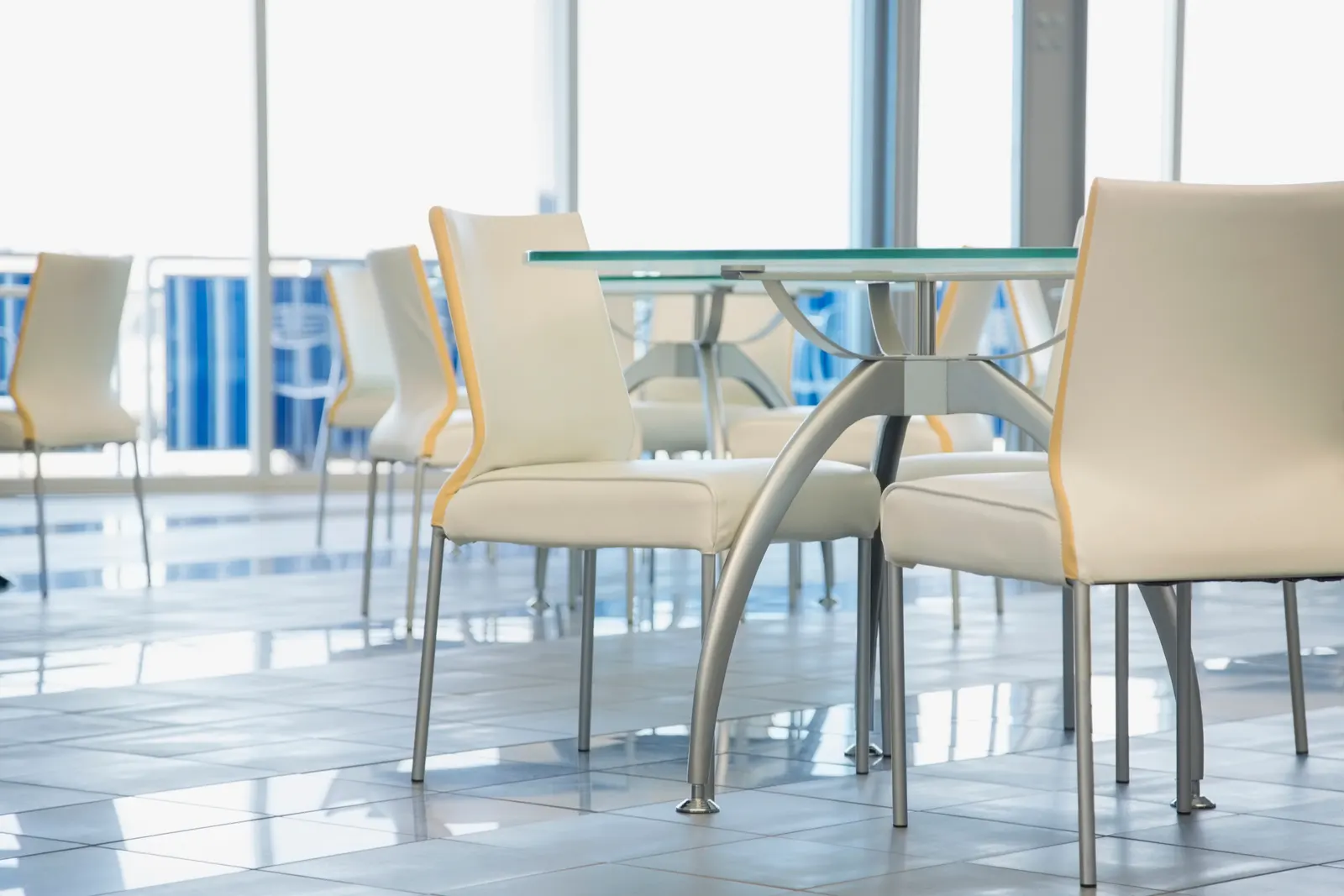 Round glass-top tables on metal bases with white leather chairs in a bright sunlit dining area.