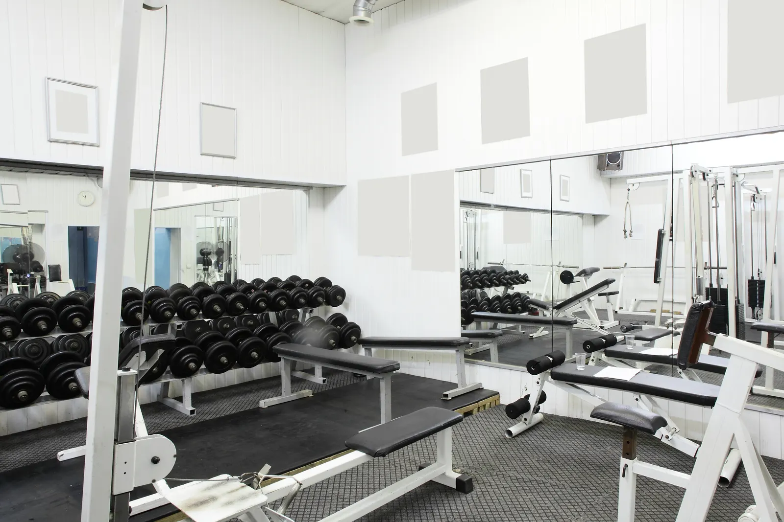 A gym with full wall mirrors reflecting racks of dumbbells and weight benches.