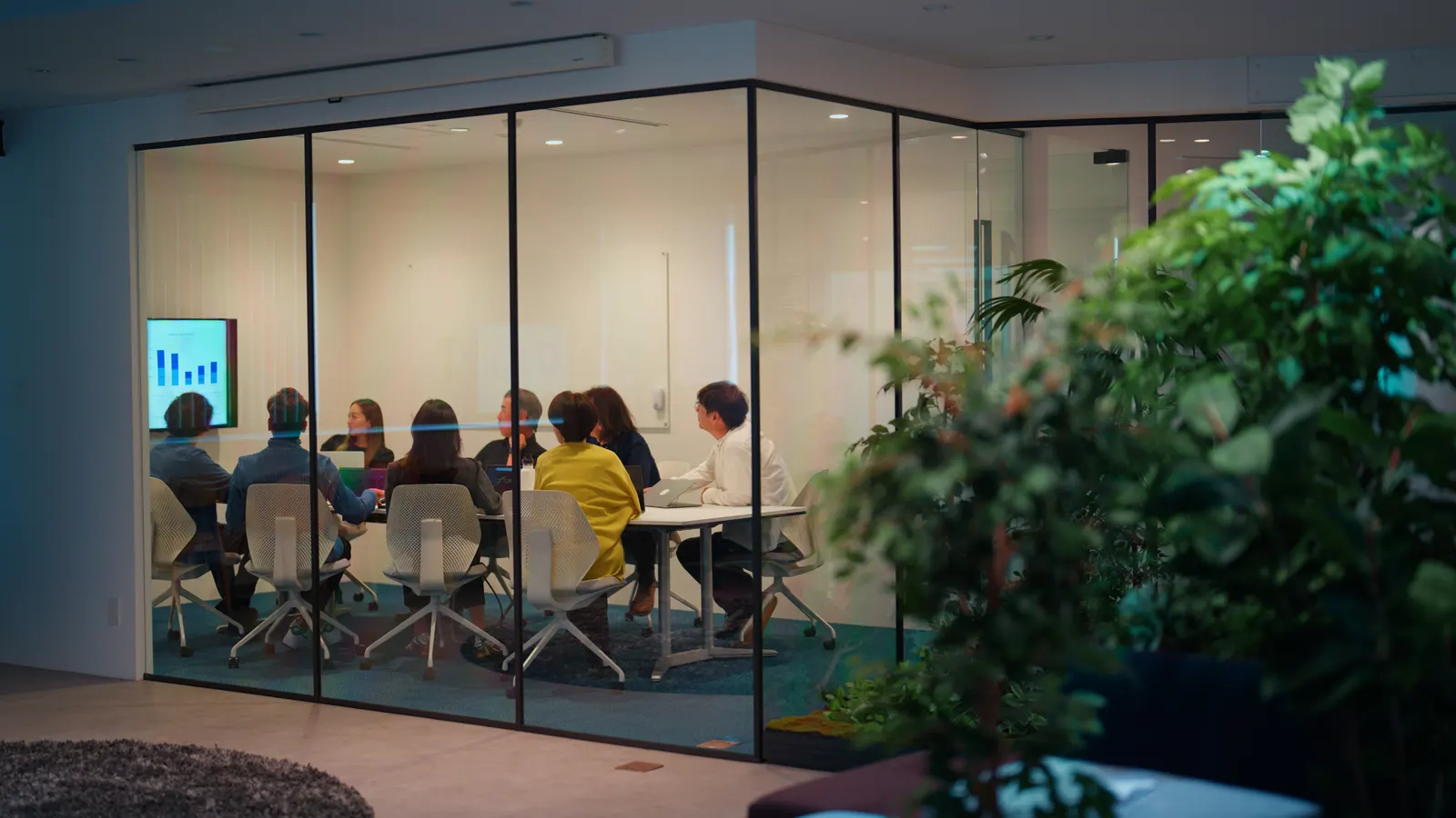 Team meeting inside a glass-enclosed conference room lit at dusk.