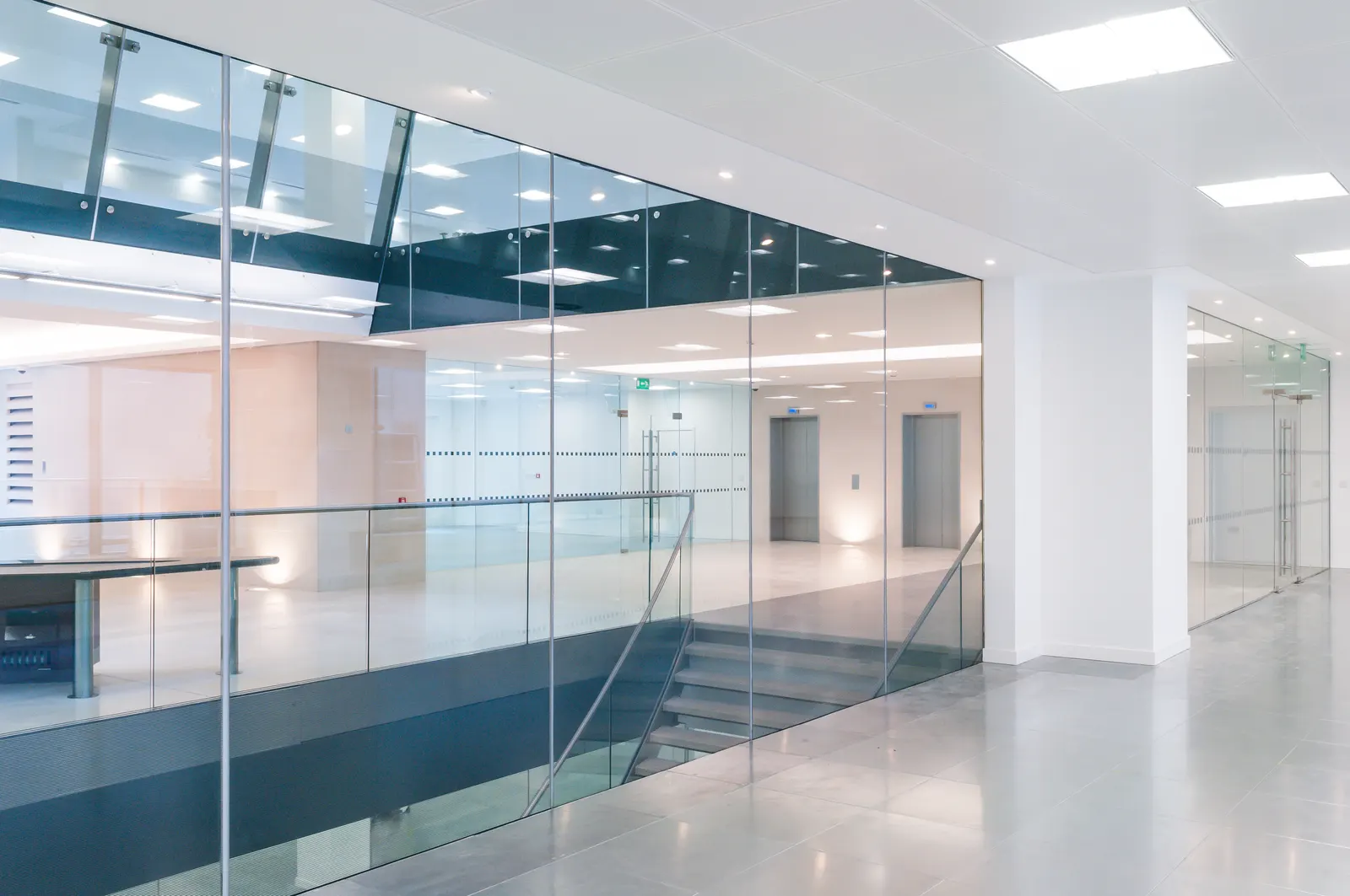 Glass partition walls and a glass balustrade around a bright office stairwell.