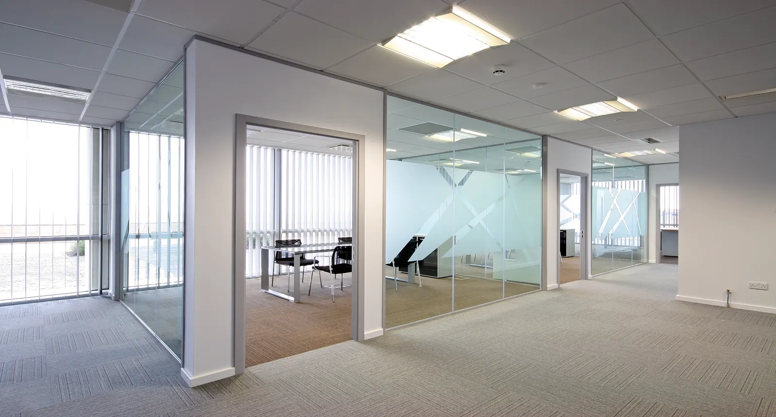 Empty office divided by frameless glass partition walls with frosted graphics.