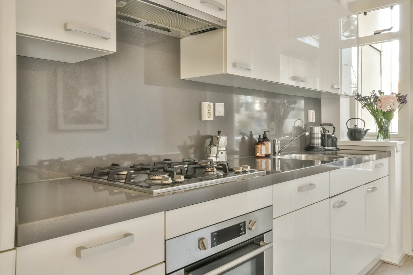 Silver speckled glass backsplash behind a gas cooktop in a white kitchen.