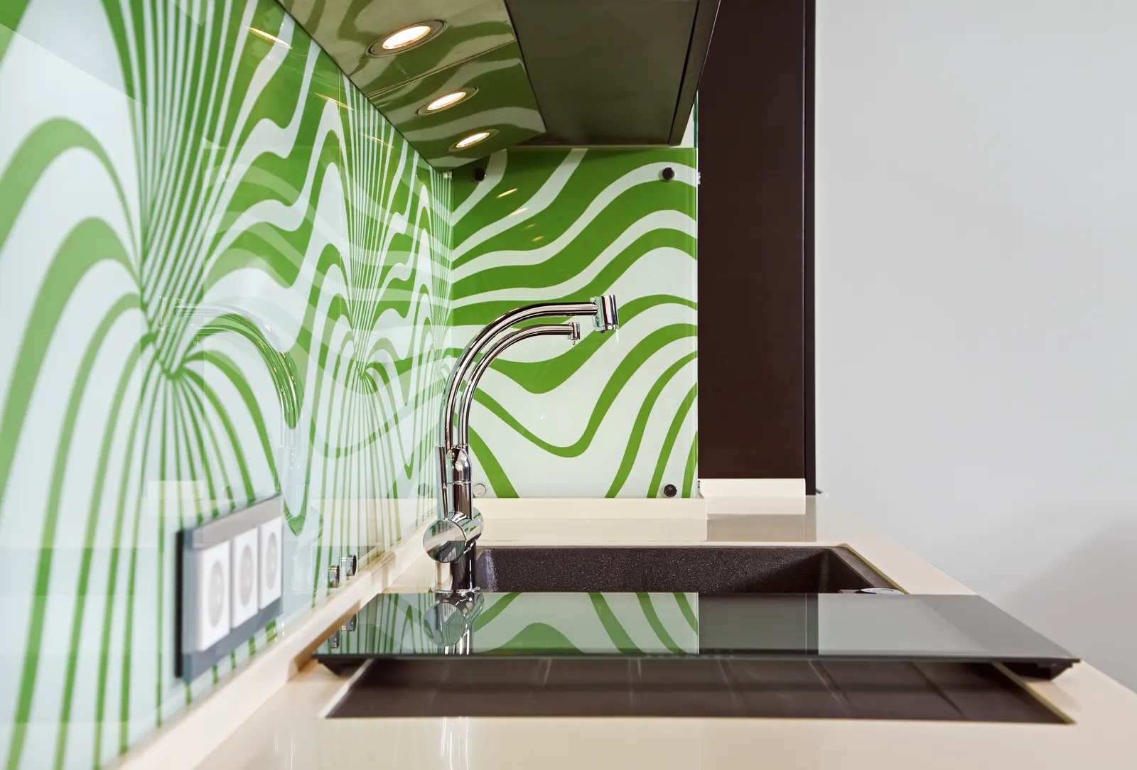 Green wave-patterned printed glass backsplash behind a kitchen sink.