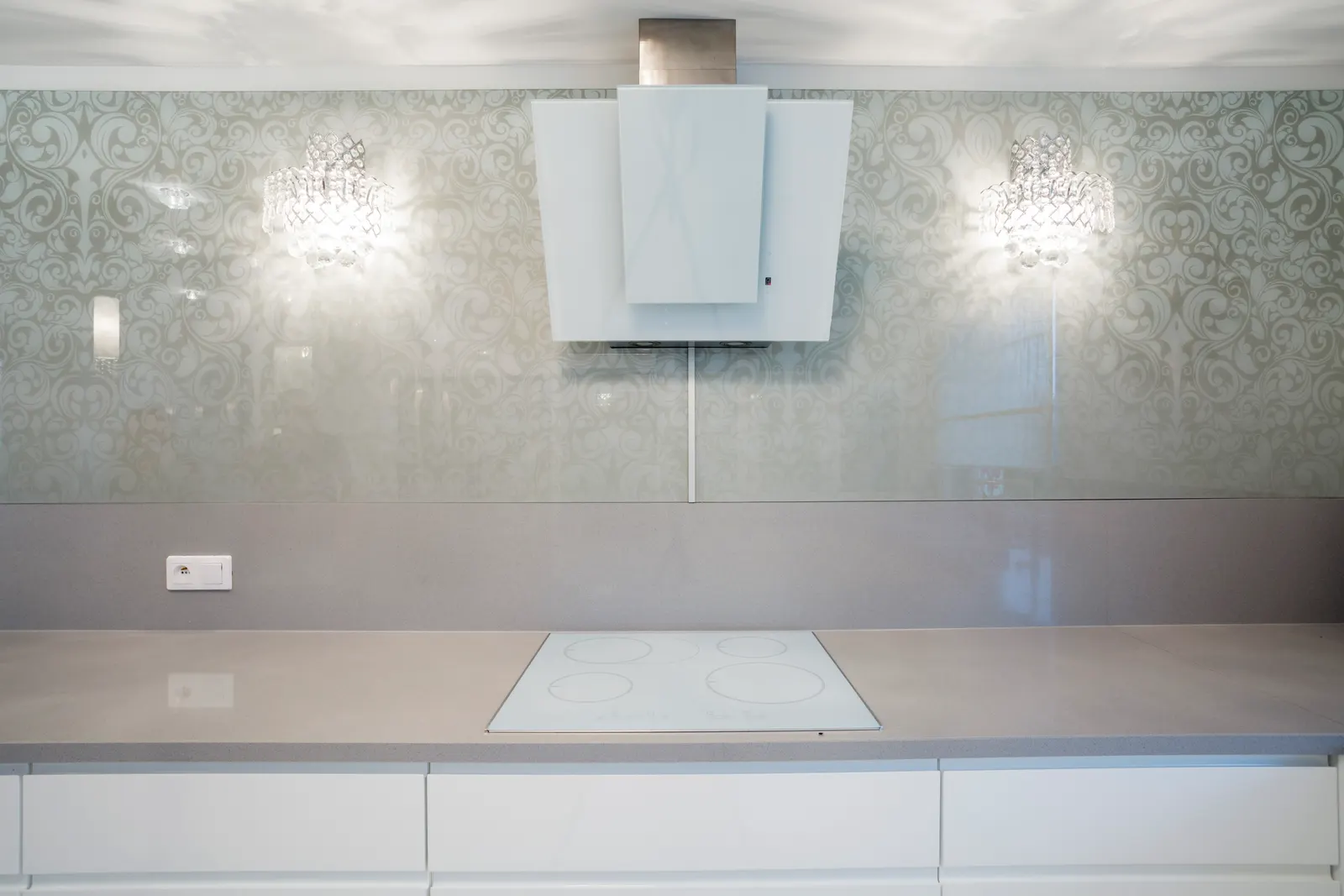 Patterned printed glass backsplash panel behind a cooktop with wall sconces.