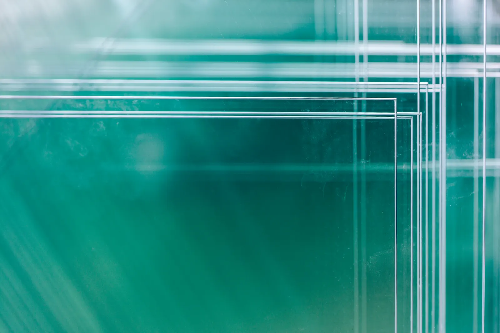 Stacked clear glass sheets showing green edges against a green background.