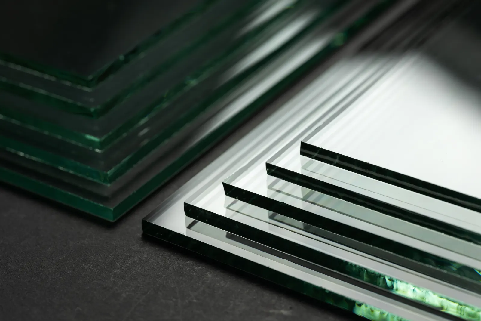 Corners of clear glass sheets of varying thickness on a dark surface.