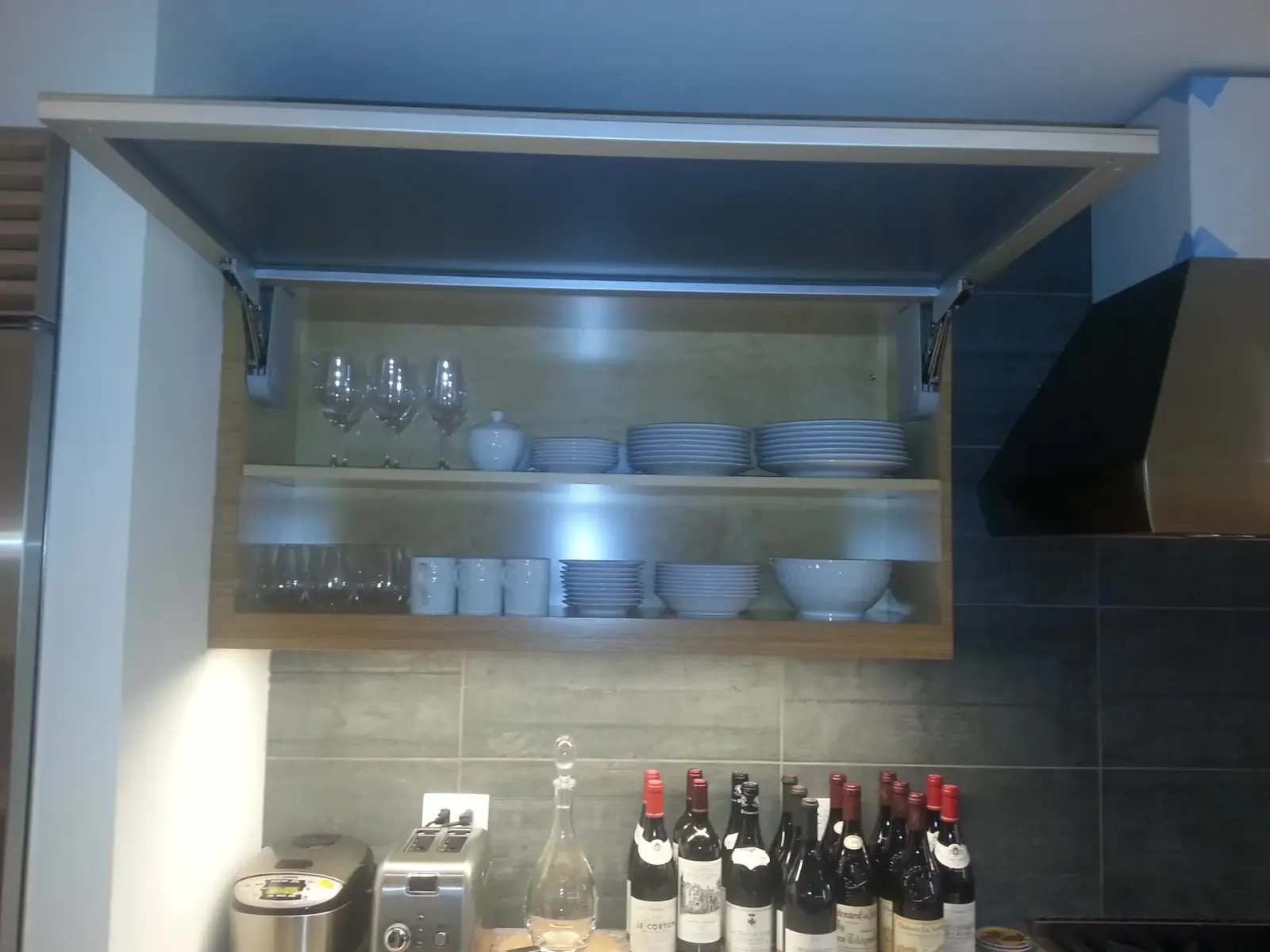 Lift-up glass-front kitchen cabinet displaying glassware.